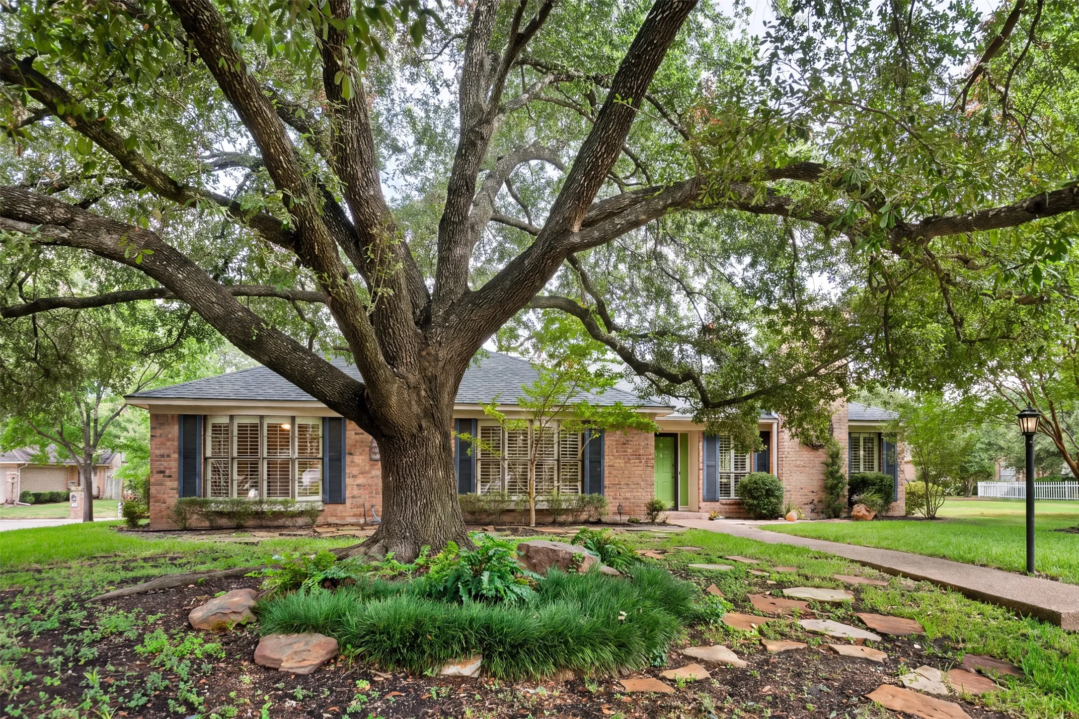 Brick exterior residence with a shingled roof and prominent mature tree