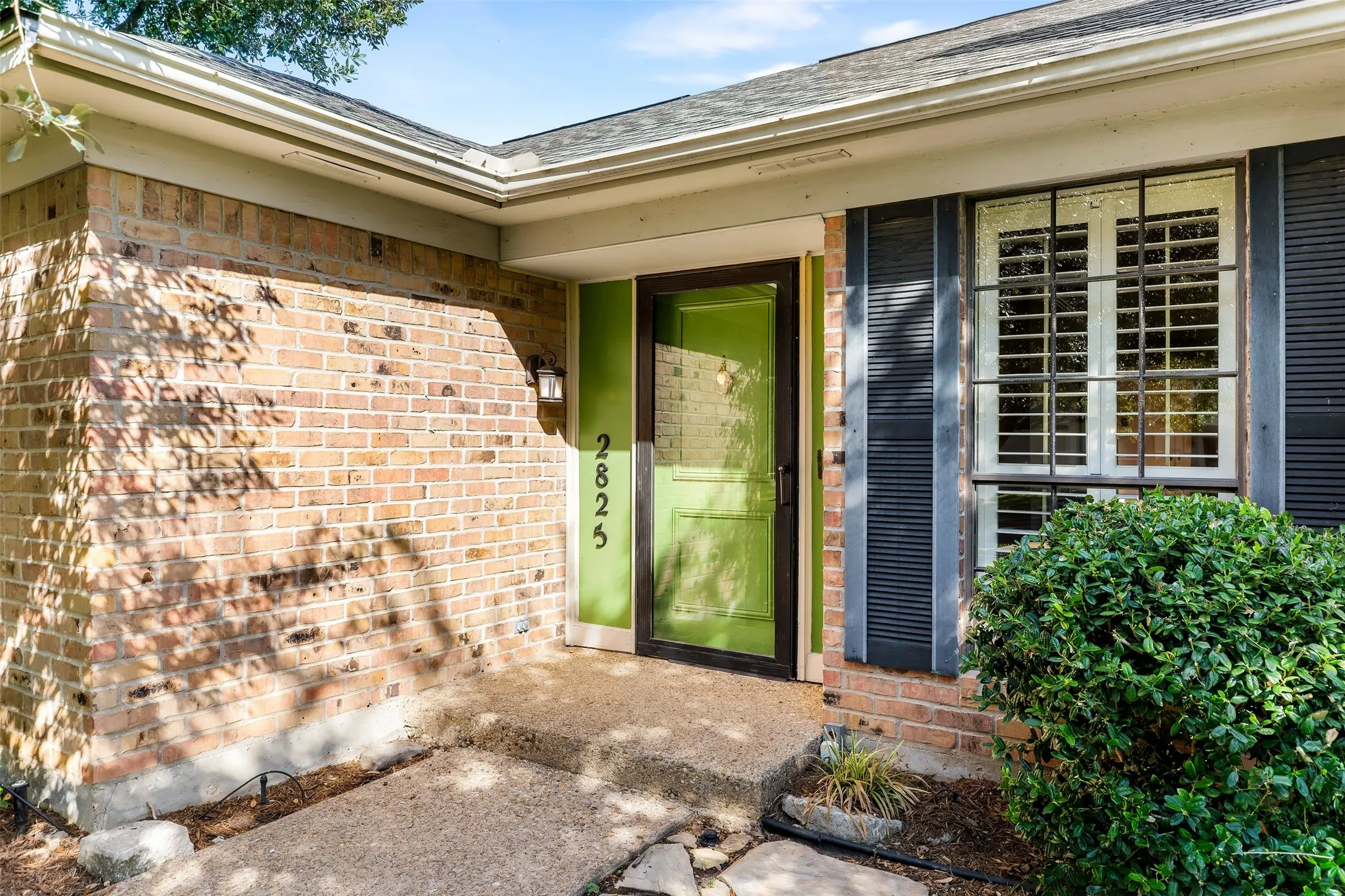 Brick exterior with a vibrant green door, dark window shutters, and a covered entry