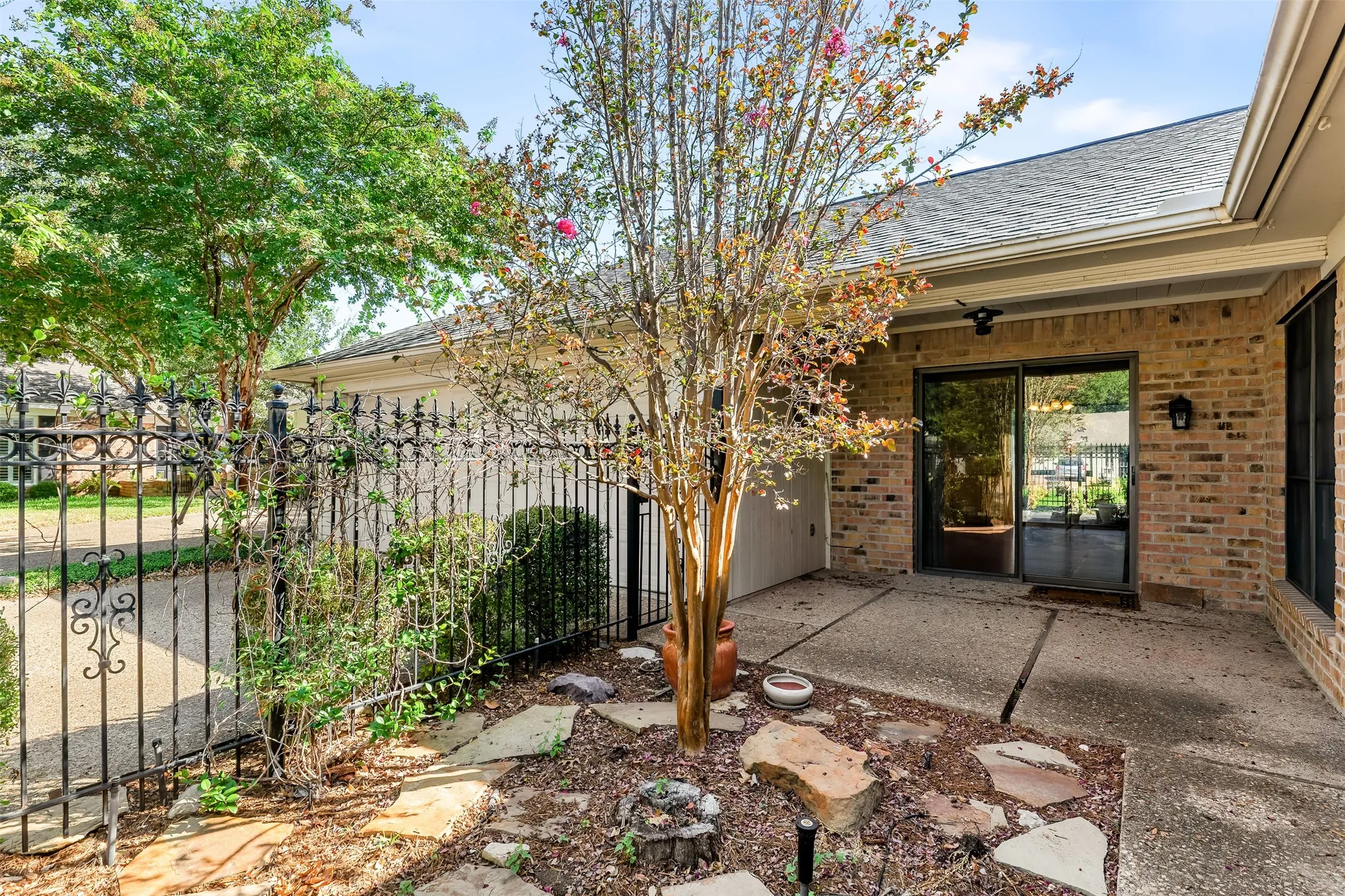 Brick exterior with a covered patio, sliding glass doors, and an ornamental iron fence