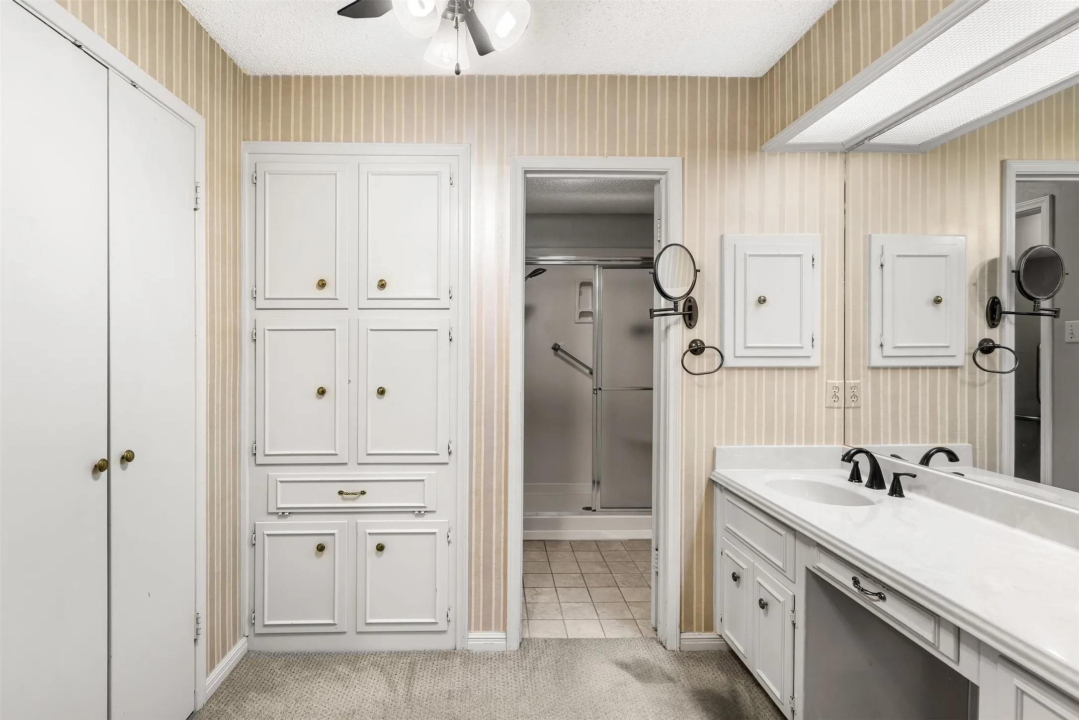 White vanity with dual integrated sinks, an expansive wall mirror, and dedicated built-in storage