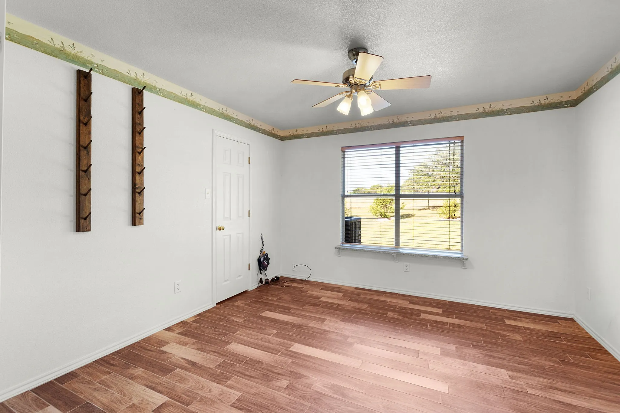 Bright interior space featuring wood-finish flooring, a window with blinds, and a ceiling fan with integrated lighting