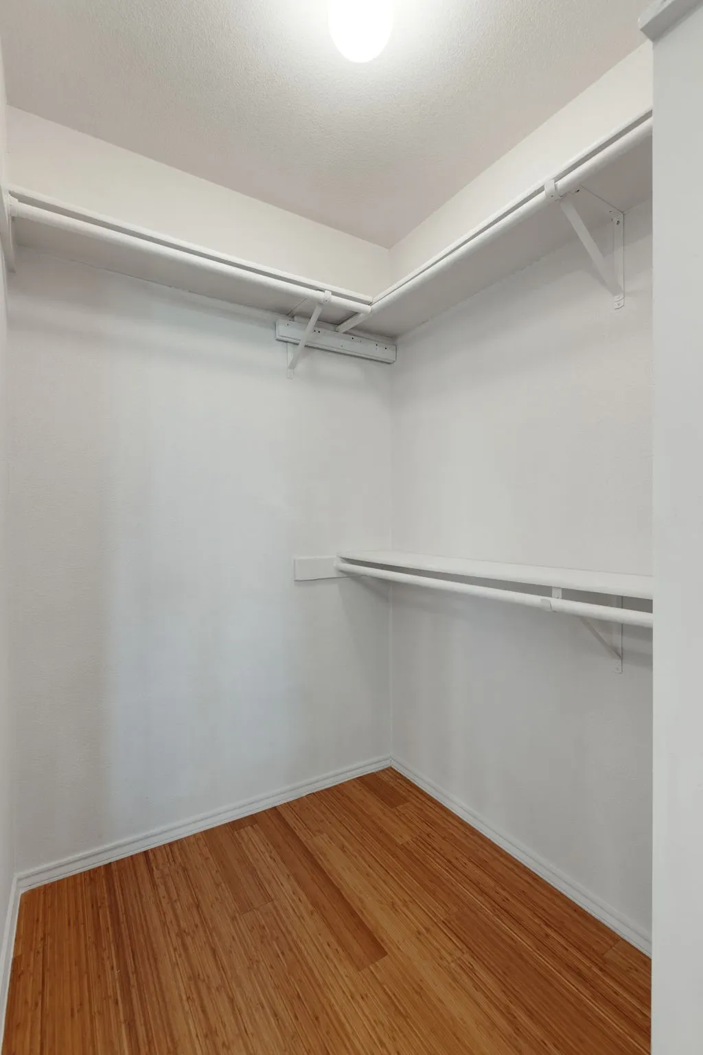 Walk-in closet featuring wood-finish flooring, white walls, built-in shelving, and integrated hanging rods