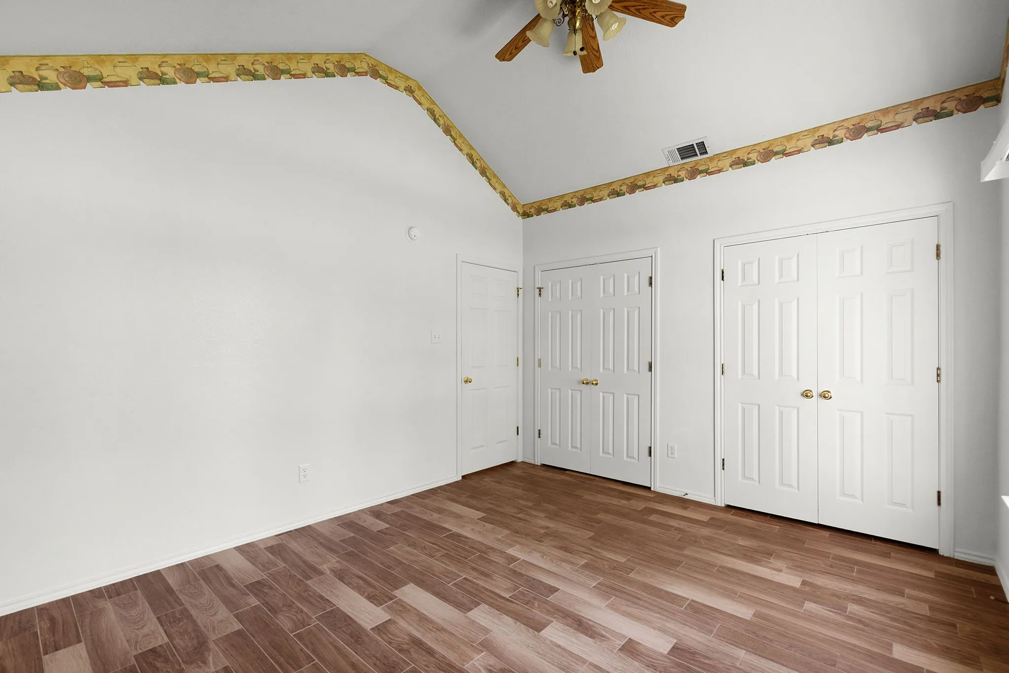 Spacious room featuring vaulted ceilings, wood-finish flooring, white walls, and two sets of bi-fold closet doors