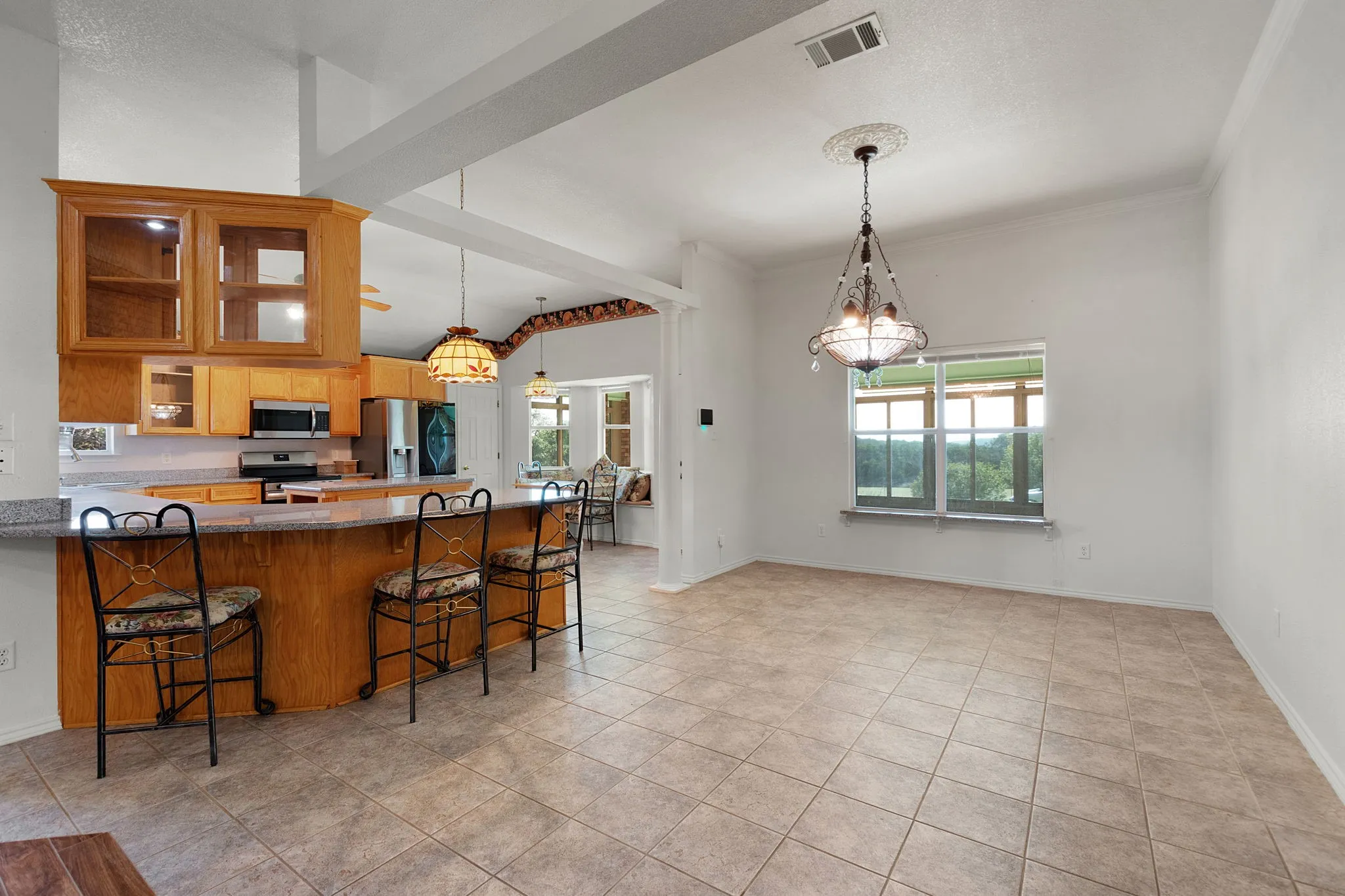 Spacious room with tile flooring, featuring an integrated kitchen with wood cabinetry and a breakfast bar