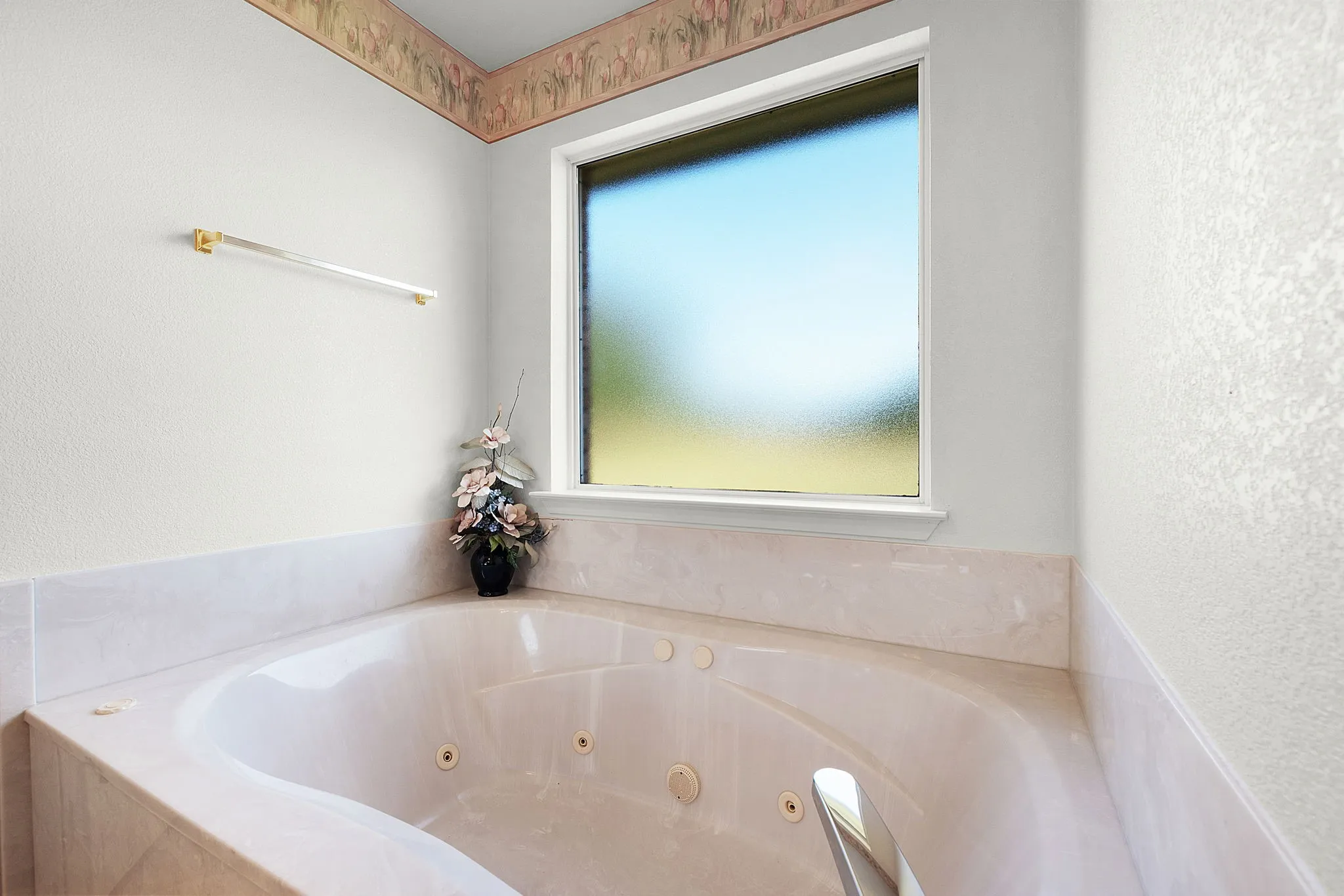 Corner jetted tub set within a tiled surround, featuring a large privacy window and textured wall finishes