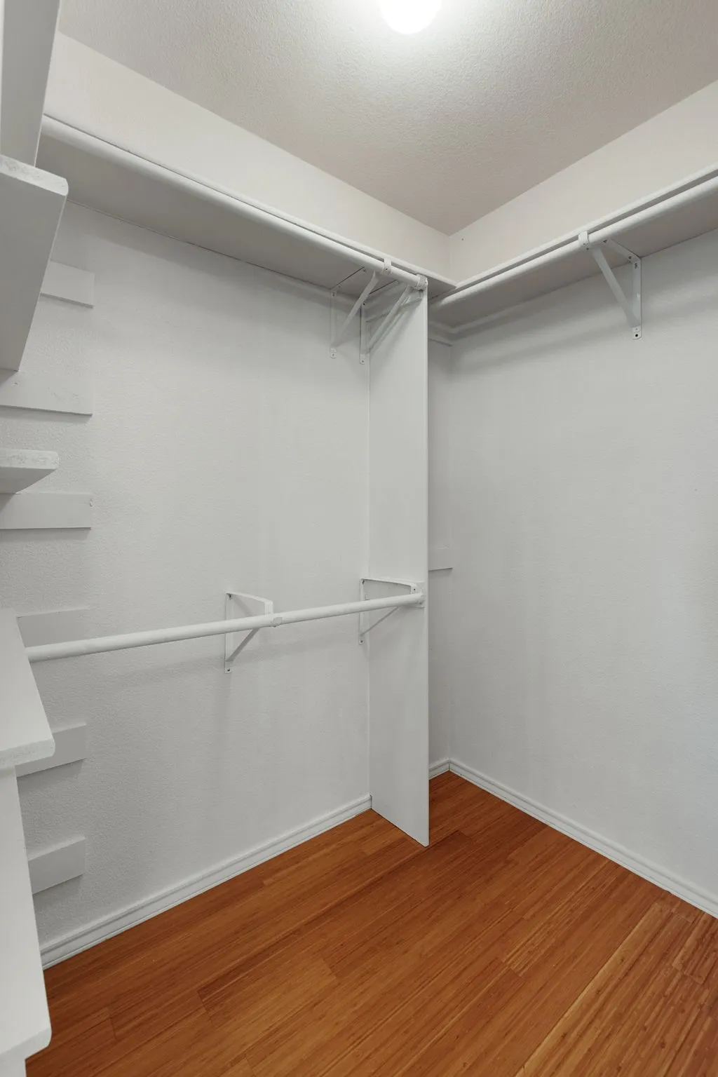 Spacious closet with wood-finish flooring, white walls, and built-in shelving and hanging rods