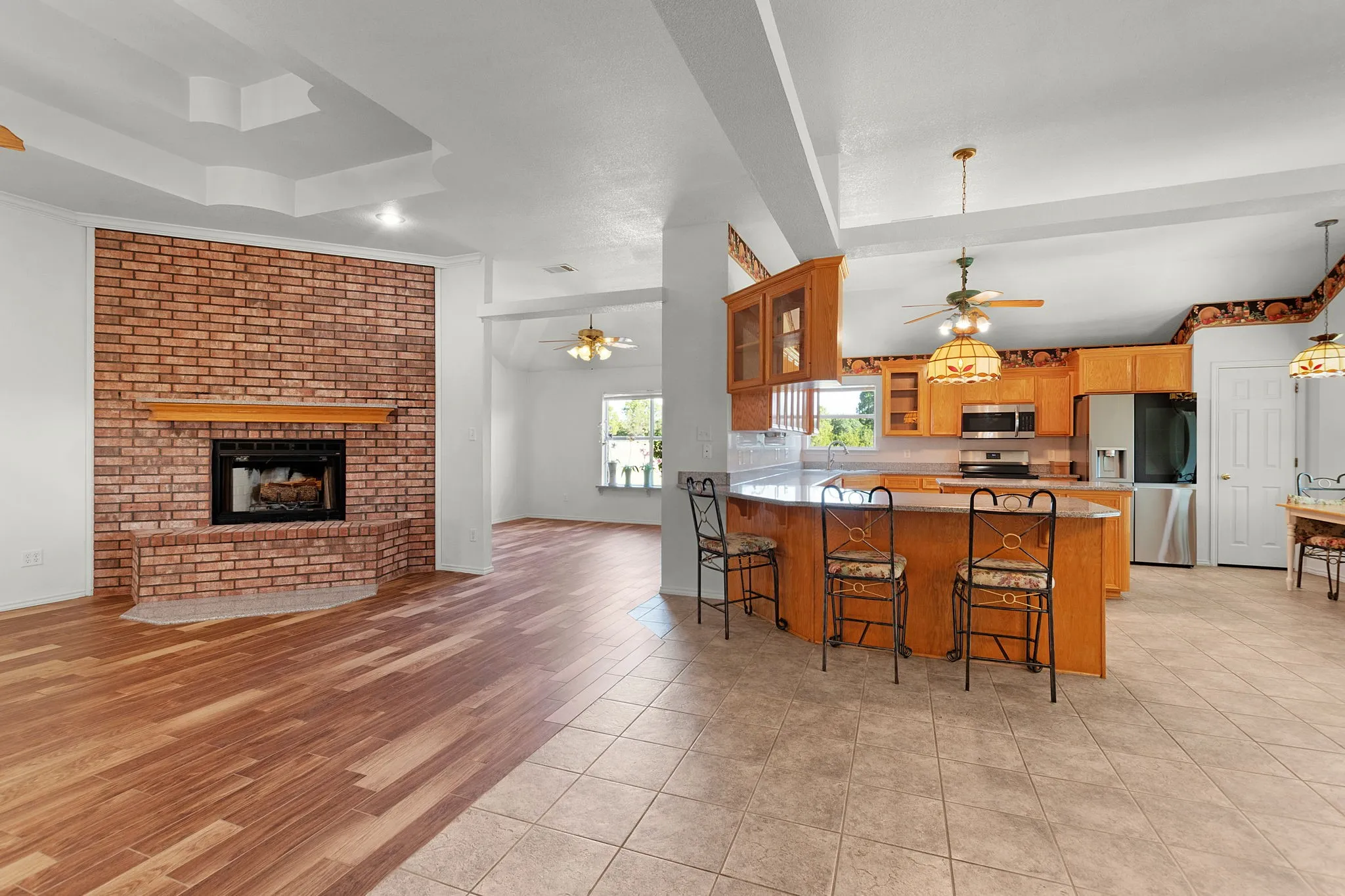 Open-concept living area featuring a brick fireplace with a wood mantel, wood-finish flooring, and a tray ceiling