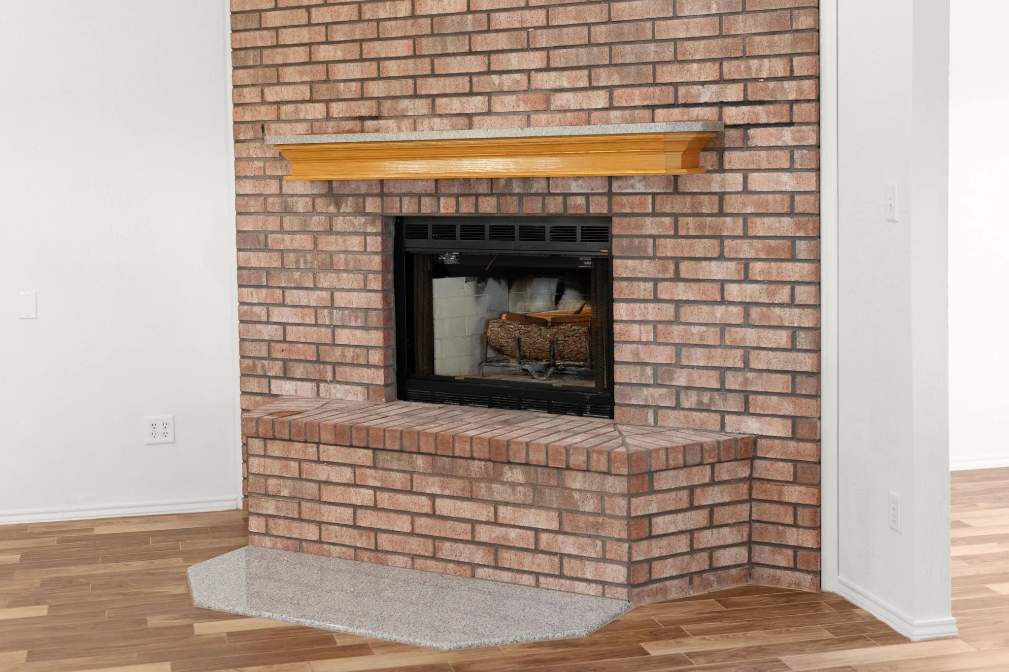 Brick fireplace with a wood mantel, black firebox, and an extended brick hearth