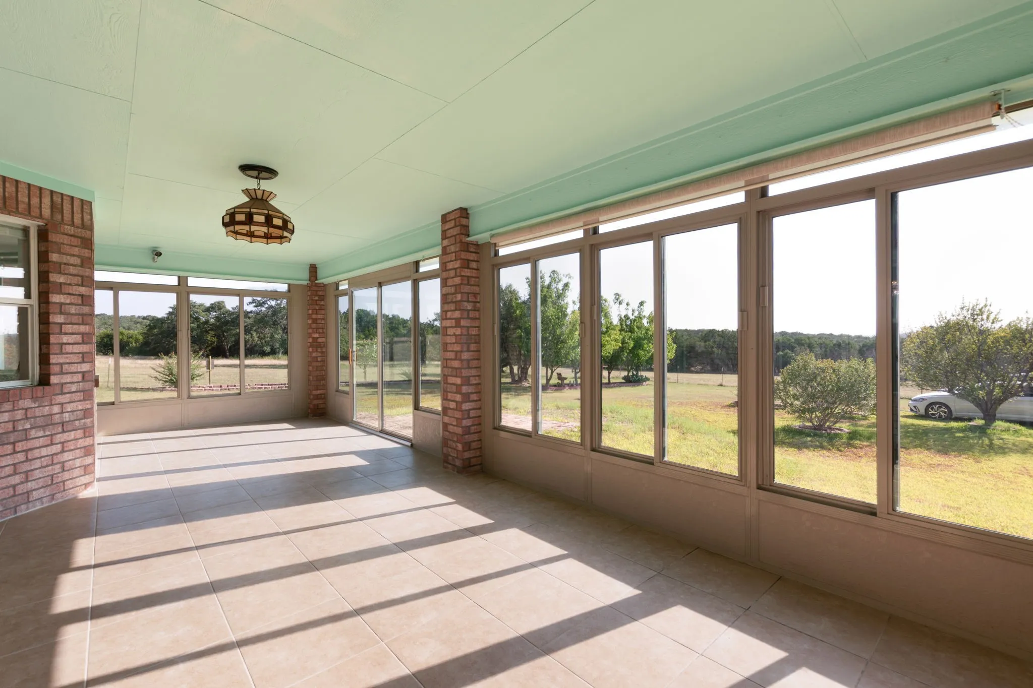 Sunroom featuring extensive window panels, tiled flooring, brick accents, and an overhead light fixture