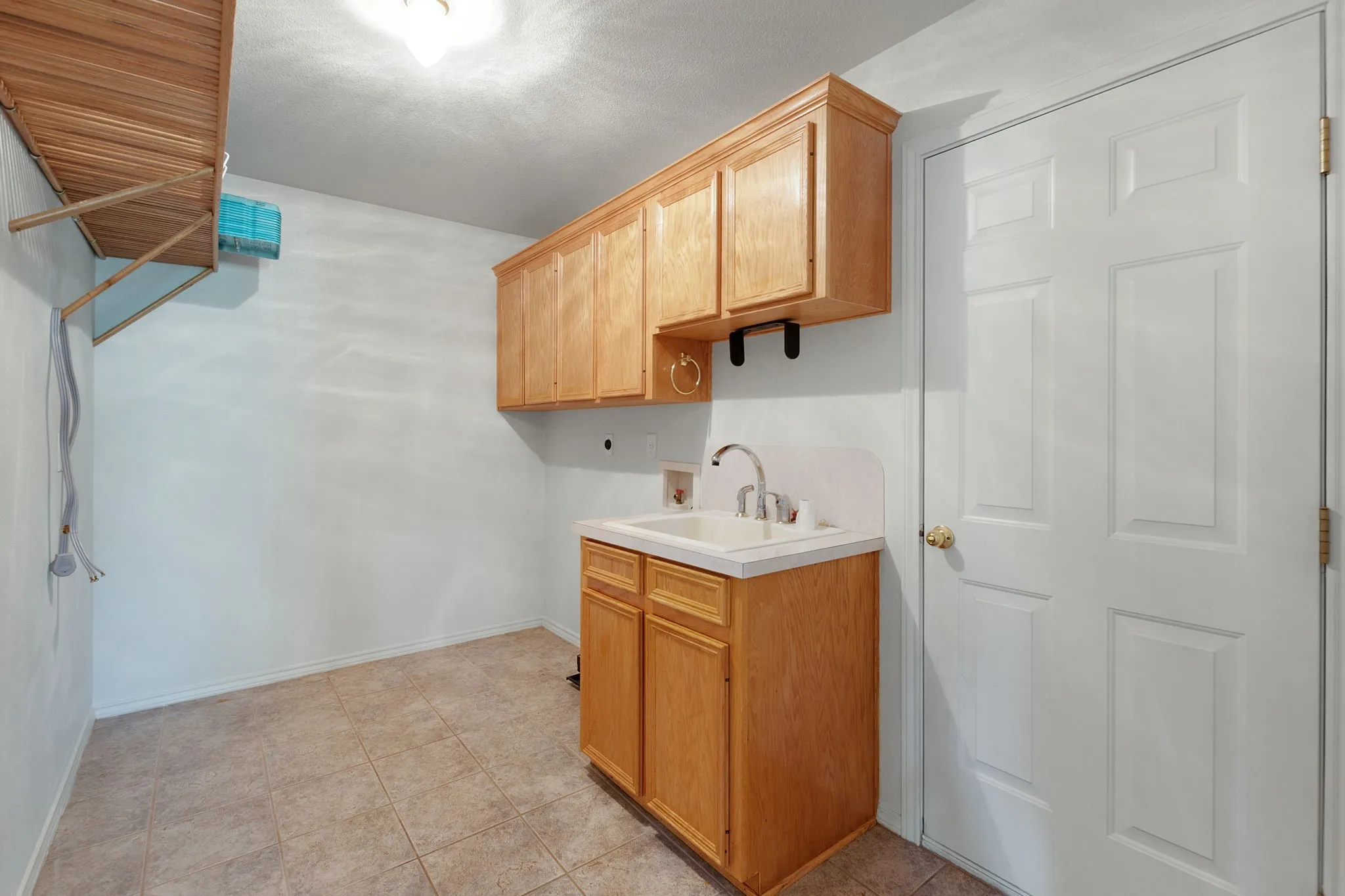 Utility room with light wood-finish cabinetry, a utility sink with a white countertop and backsplash, and tiled flooring