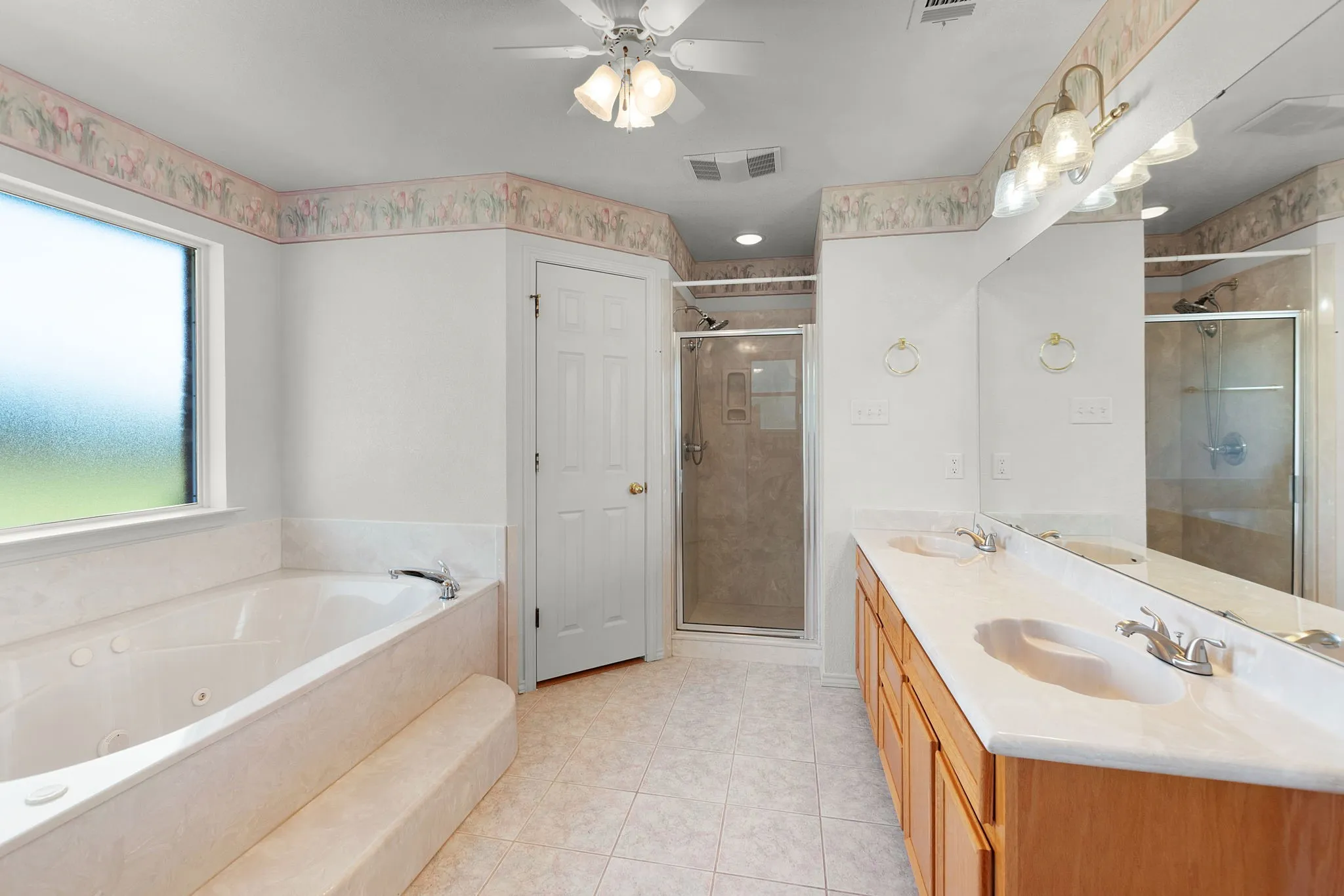Spacious bathroom featuring a dual vanity, large soaking tub with a frosted window, and a separate glass-enclosed shower