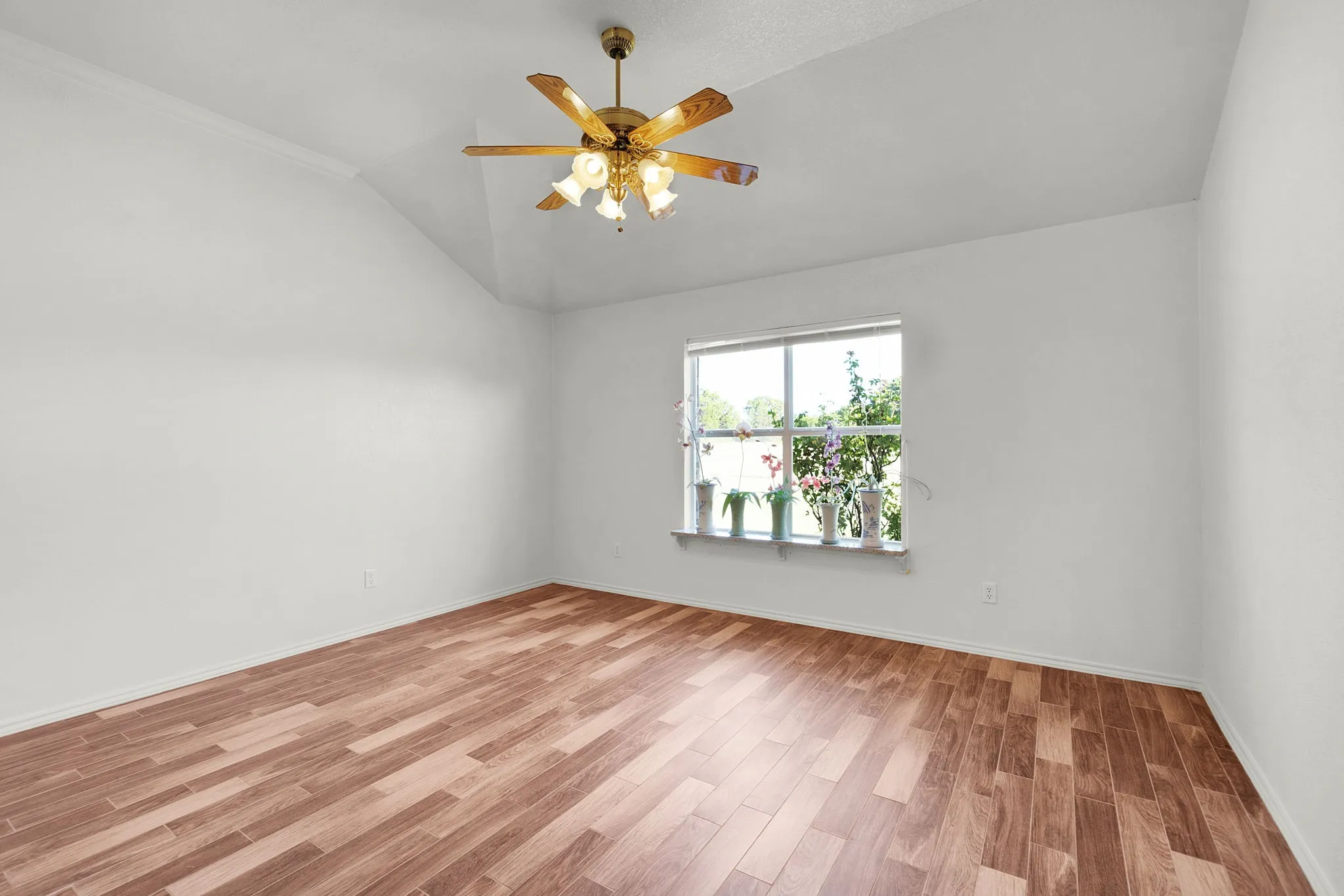Spacious room featuring vaulted ceilings, a ceiling fan with integrated lighting, wood-finish flooring, and a large window providing abundant natural light