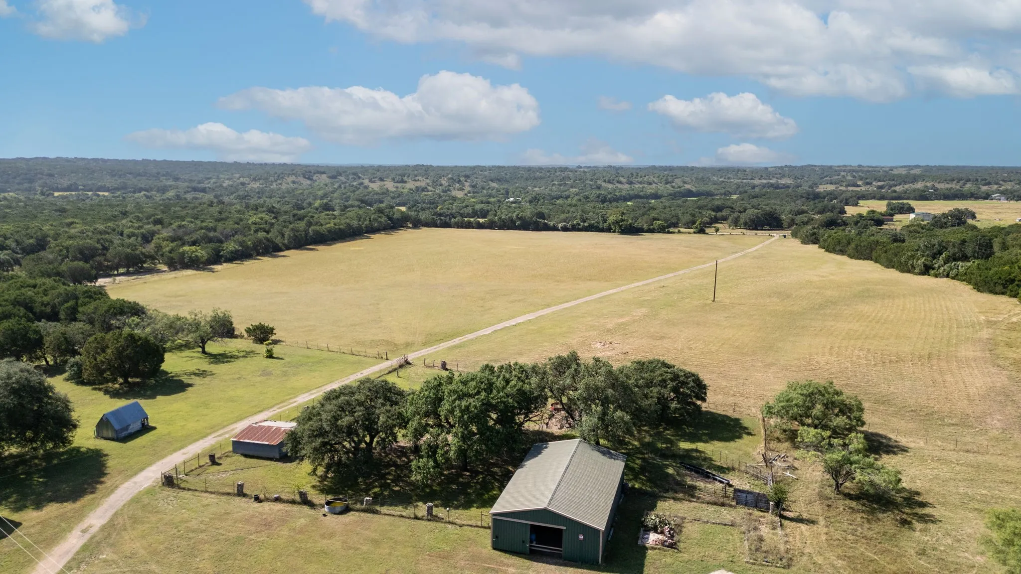 Expansive property featuring a large open field, mature tree lines, and a gravel driveway