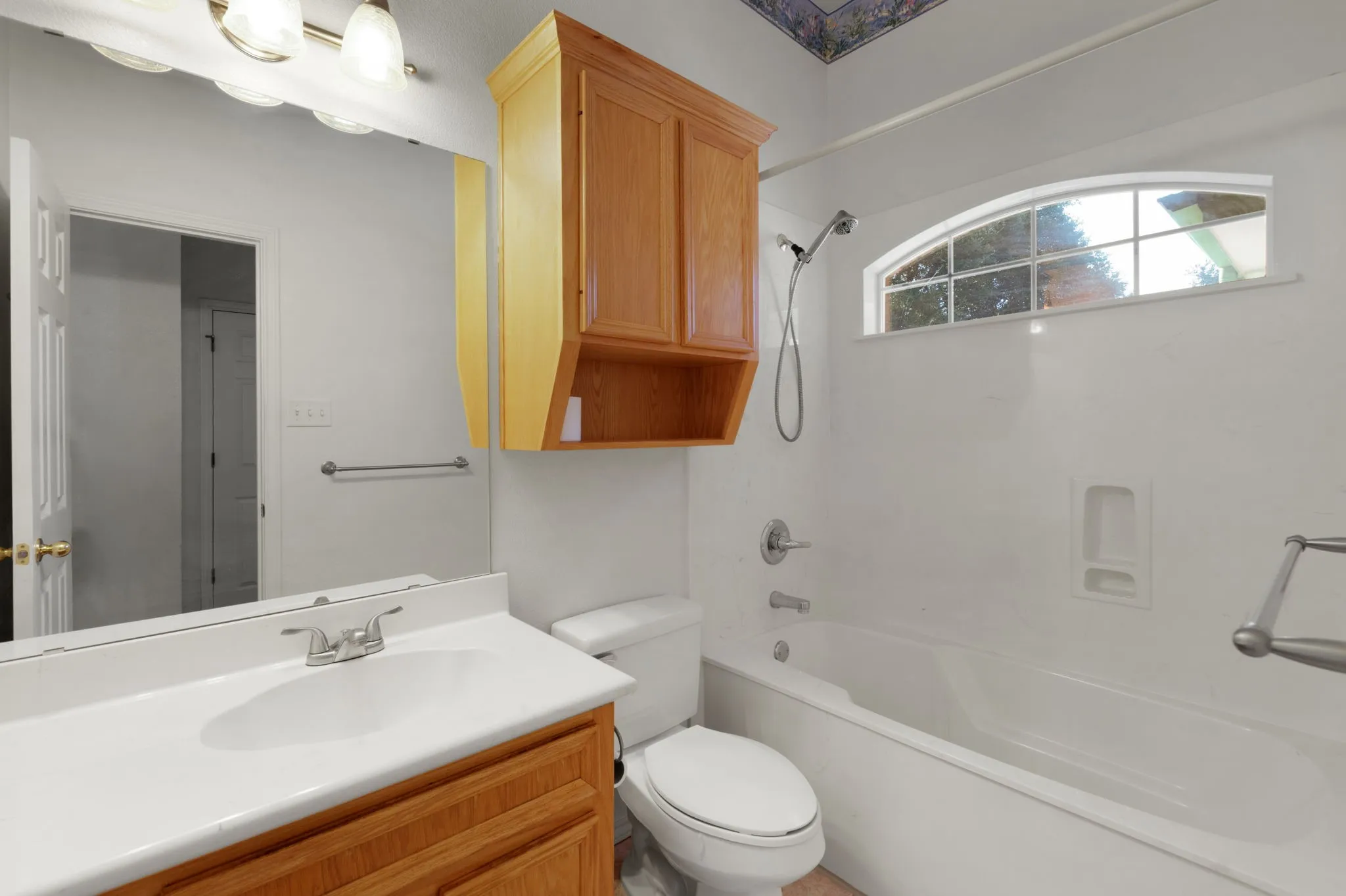 Full bathroom featuring a single vanity, a large mirror, a combination tub and shower, and a built-in wall cabinet