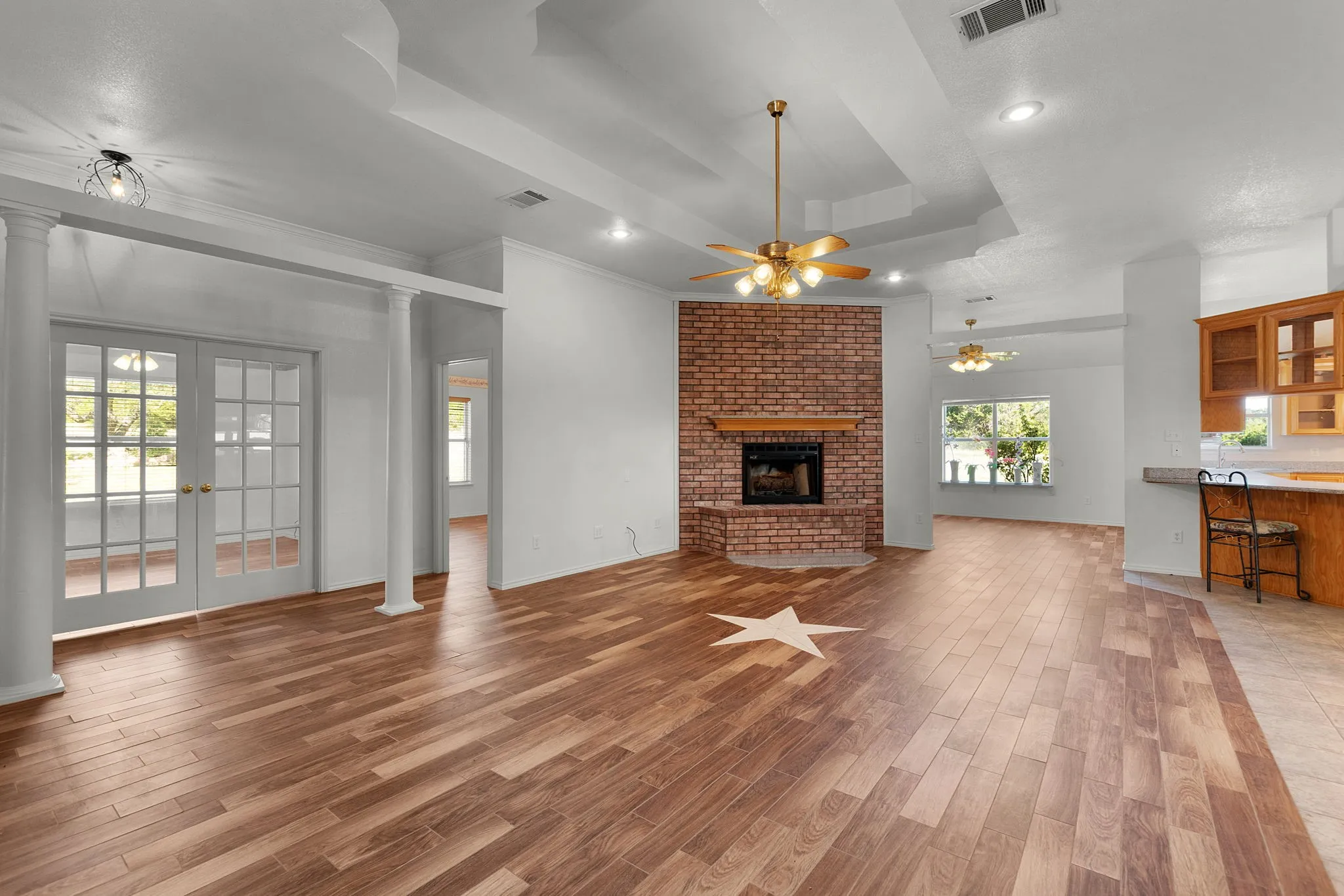 Open-concept living space featuring wood-finish flooring, a brick fireplace with a wood mantle, and a recessed ceiling with ceiling fans