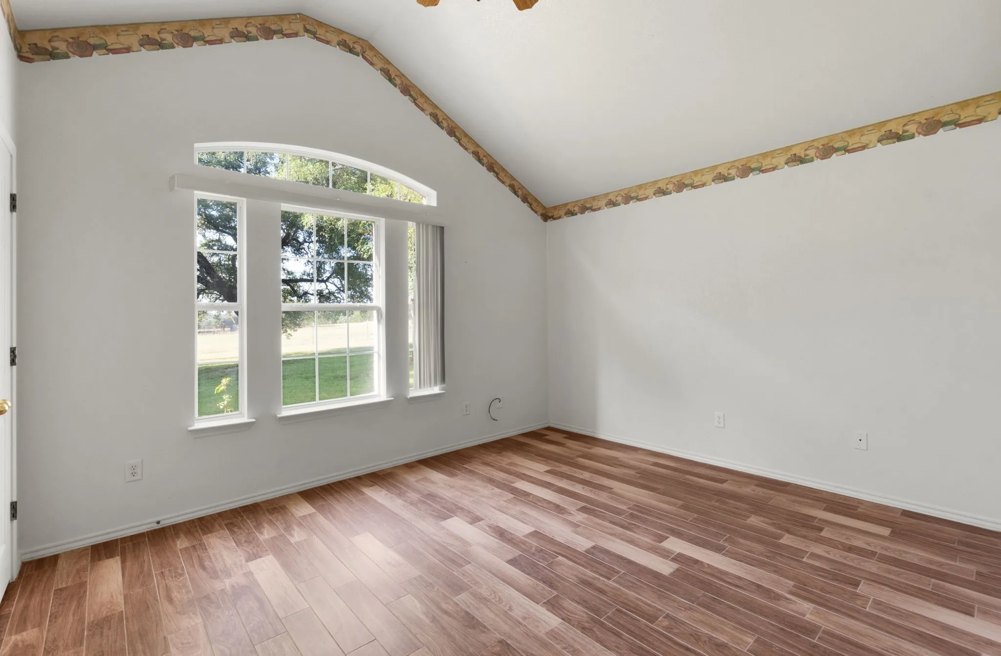 Vaulted ceiling room featuring an arched window, wood-finish flooring, and white walls