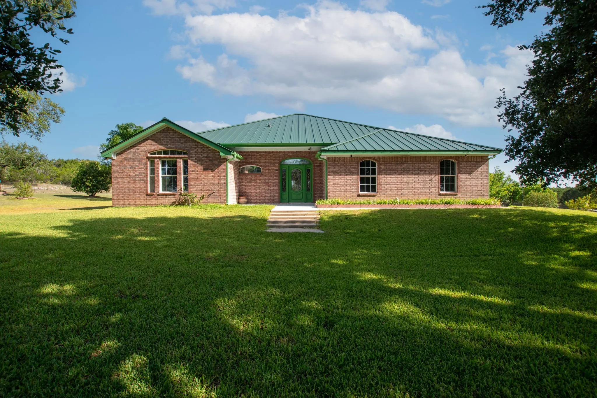 Brick exterior with a distinctive green metal roof, arched transom entry, multiple arched windows, and a tiered stone walkway