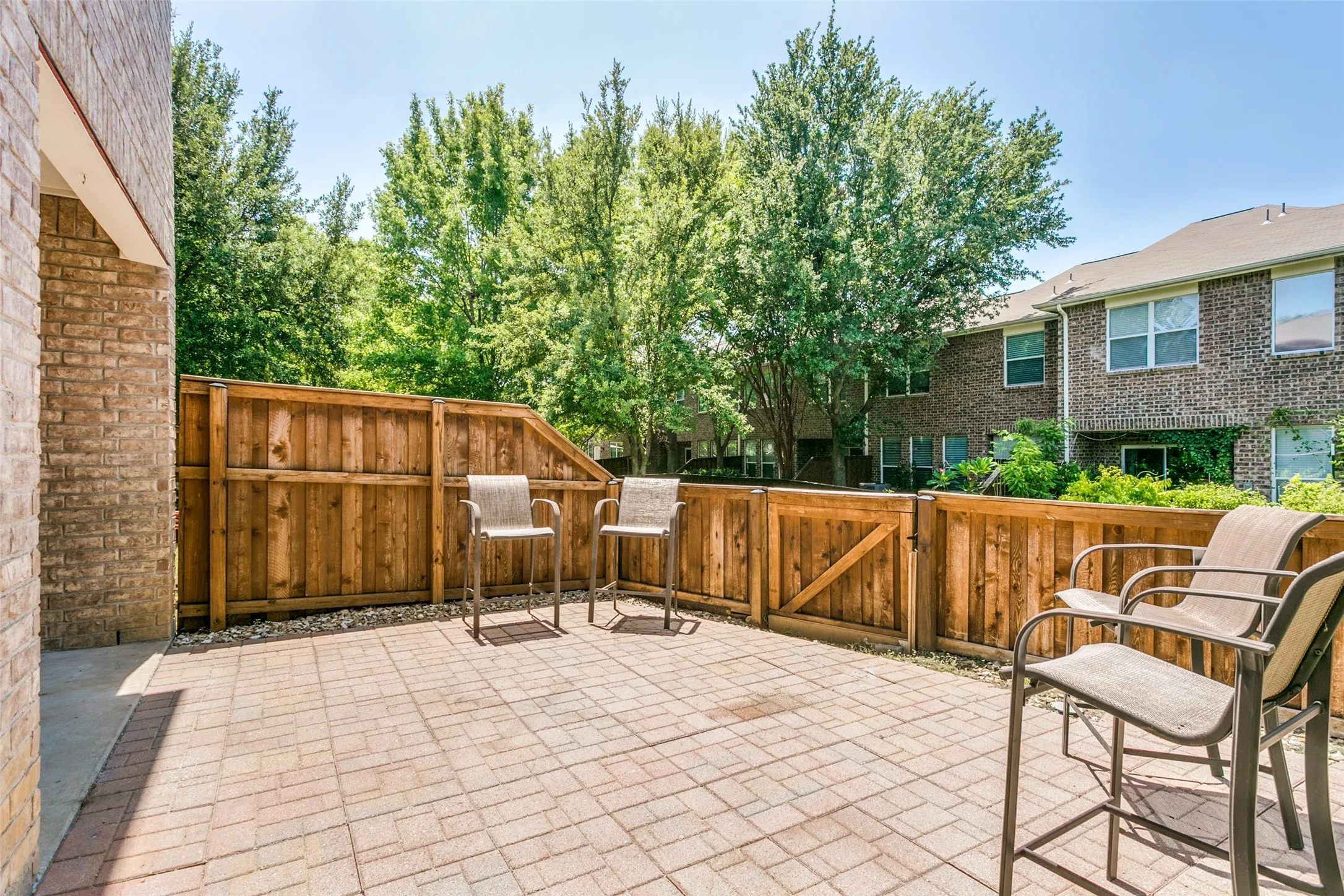 Expansive brick paver patio featuring a privacy fence, surrounding landscaping, and a brick exterior