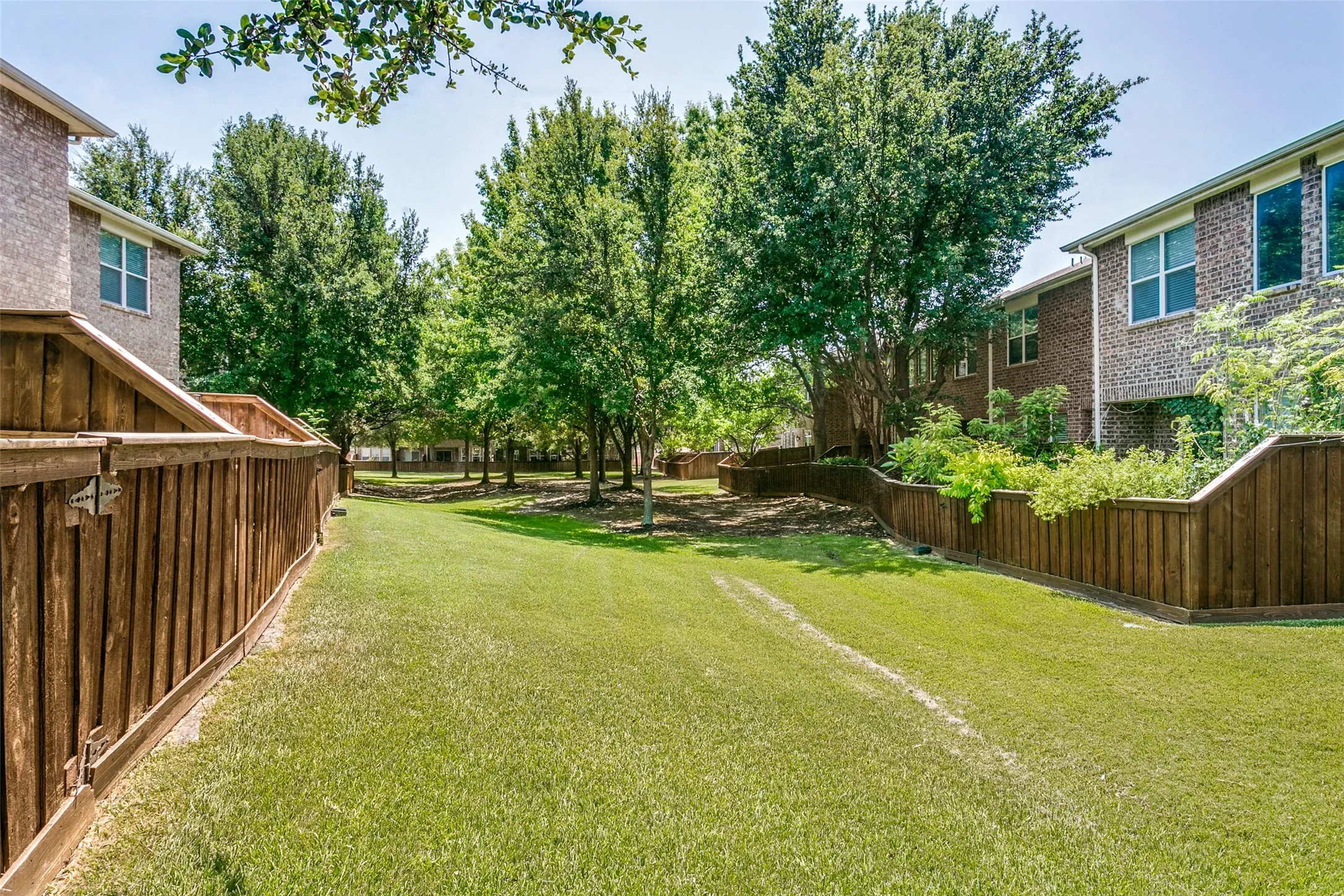 Expansive green space featuring mature trees and a wood privacy fence