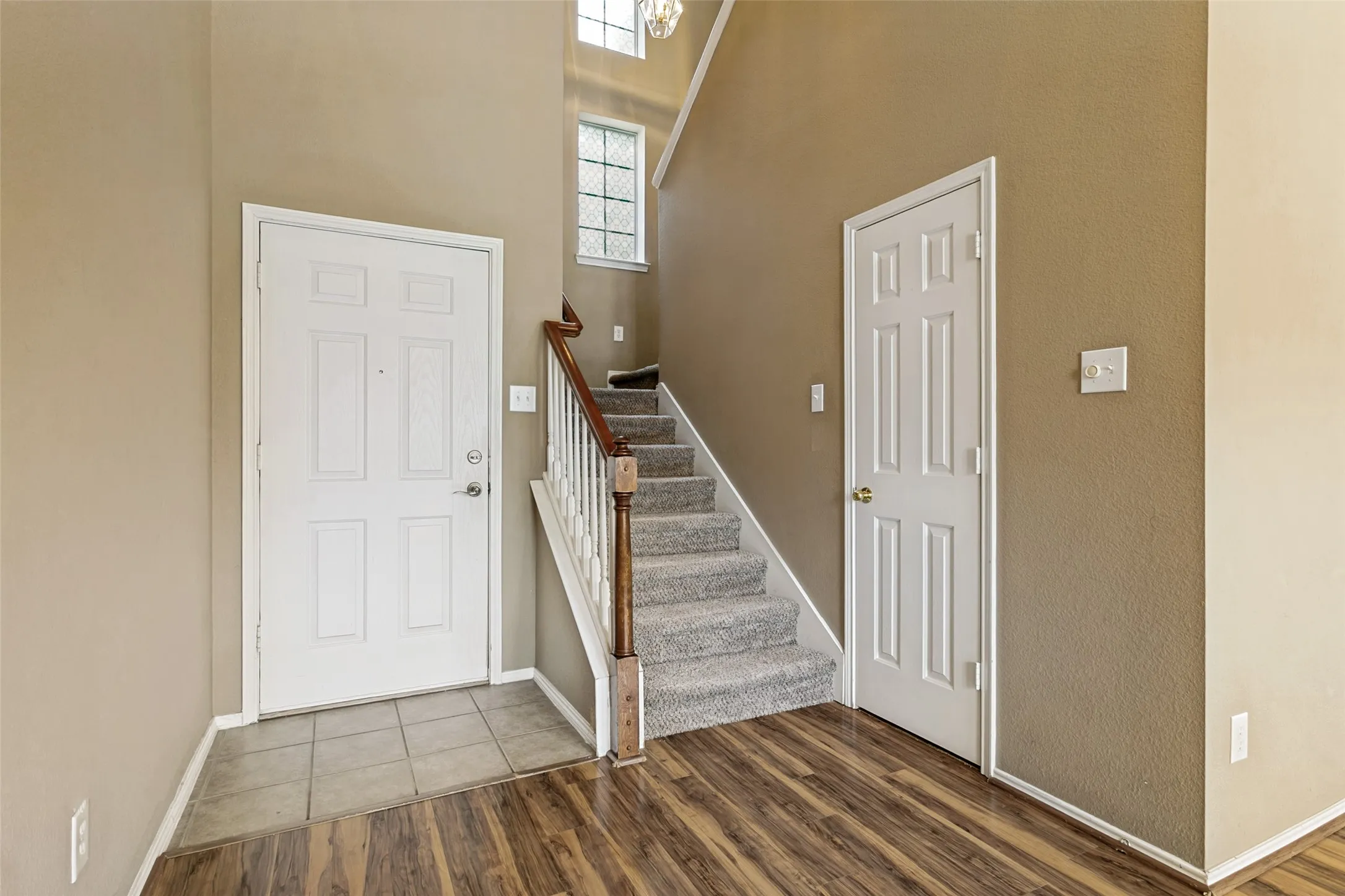 Entryway featuring a paneled door, ceramic tile flooring, Pergo flooring, a carpeted staircase with wood handrail, and a high window.