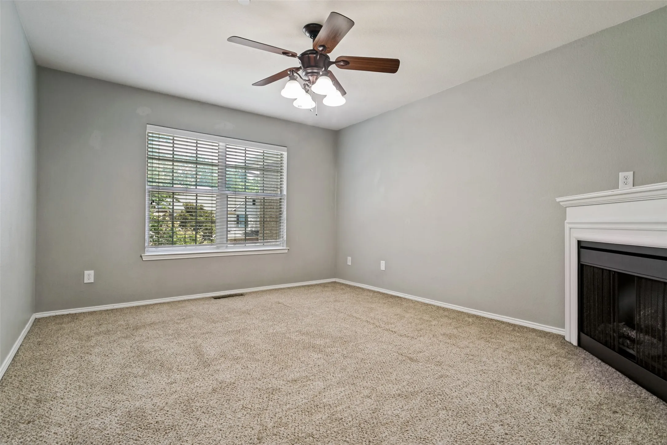 Carpeted room featuring a ceiling fan with integrated lighting, a large window with blinds, and a built-in fireplace with a white mantel