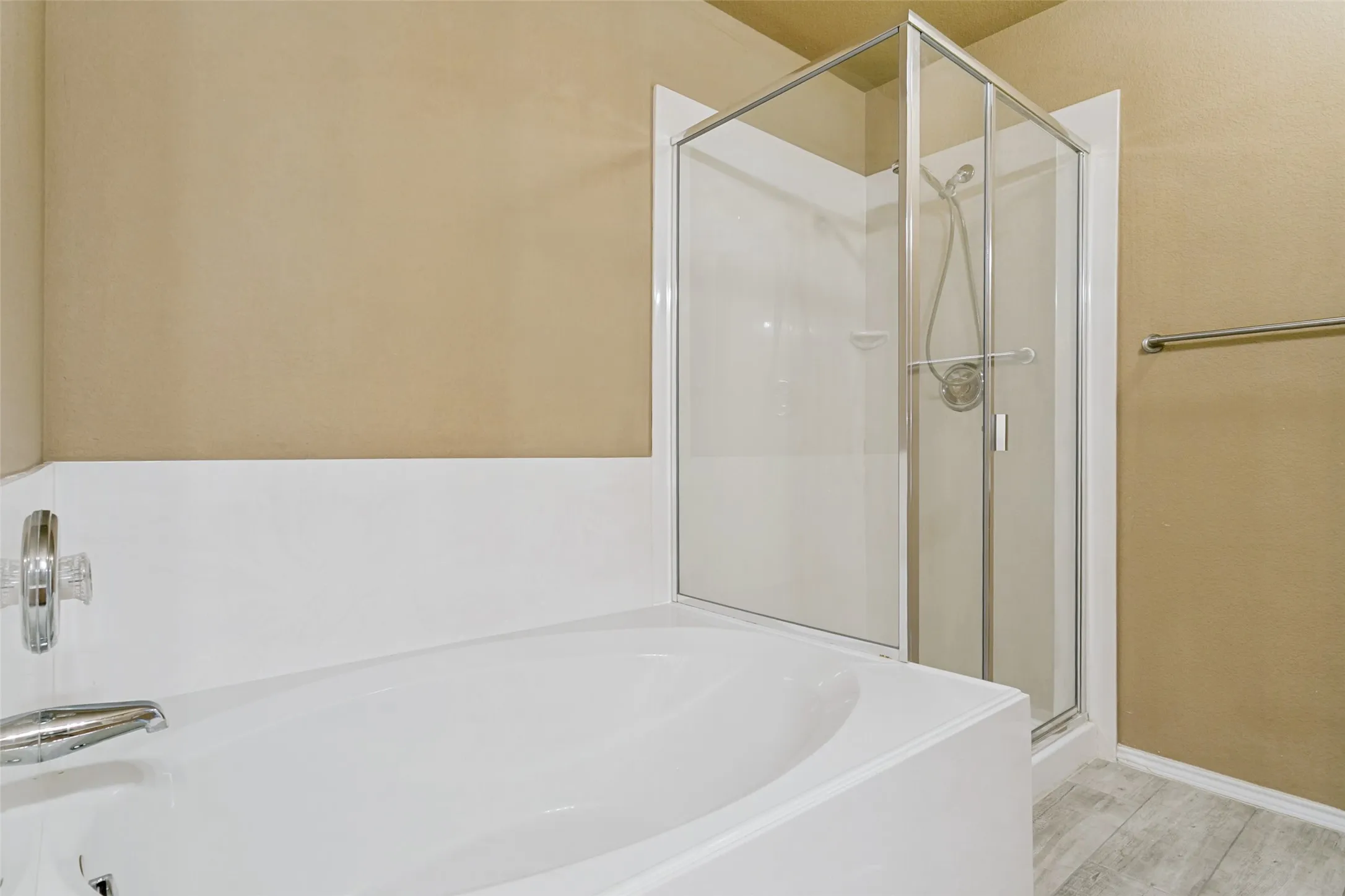 Soaking tub with chrome fixtures, glass-enclosed shower, and light wood-finish flooring