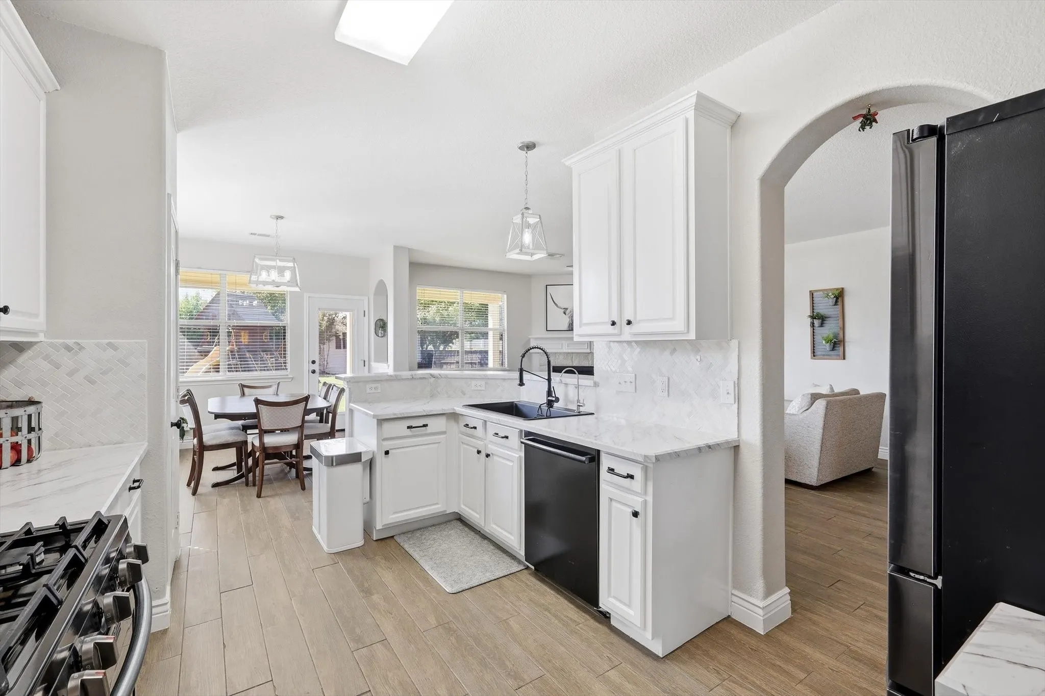 Bright kitchen featuring white cabinetry, light-toned countertops, a black sink with a matte black faucet, and a black built-in dishwasher