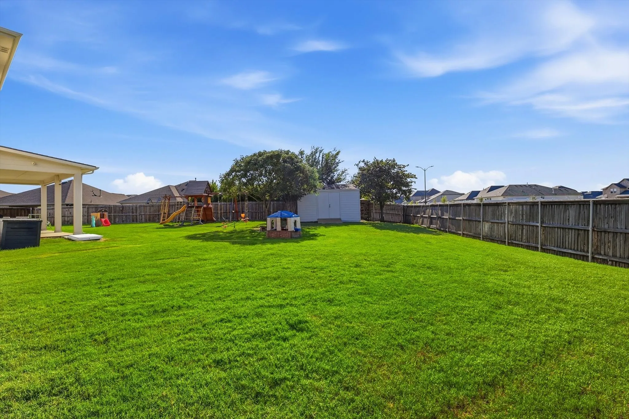 Expansive backyard featuring a large green lawn, covered patio, privacy fencing, and a white storage shed