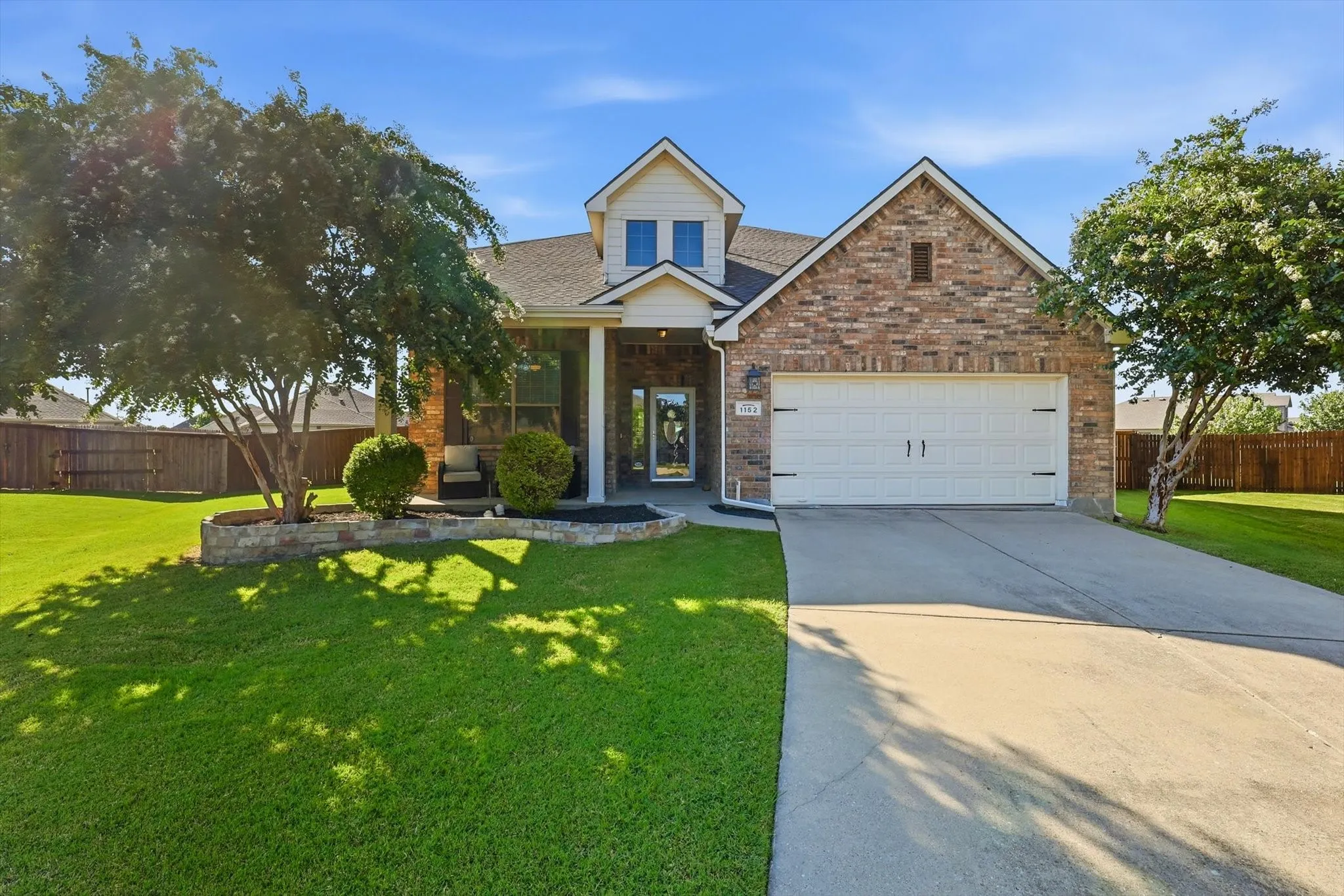 Brick and siding exterior featuring an attached two-car garage, mature landscaping, and a covered entryway