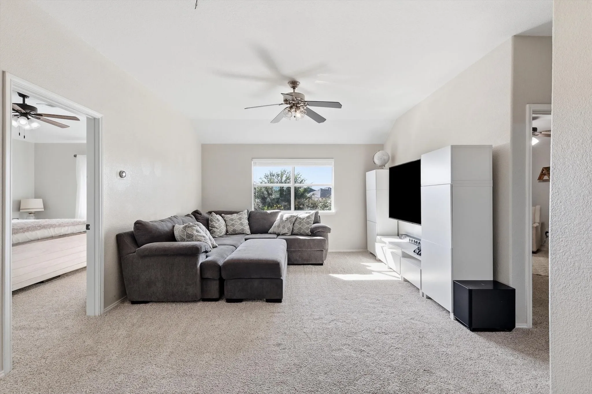 Spacious carpeted room featuring a ceiling fan, window with exterior views, and neutral wall tones