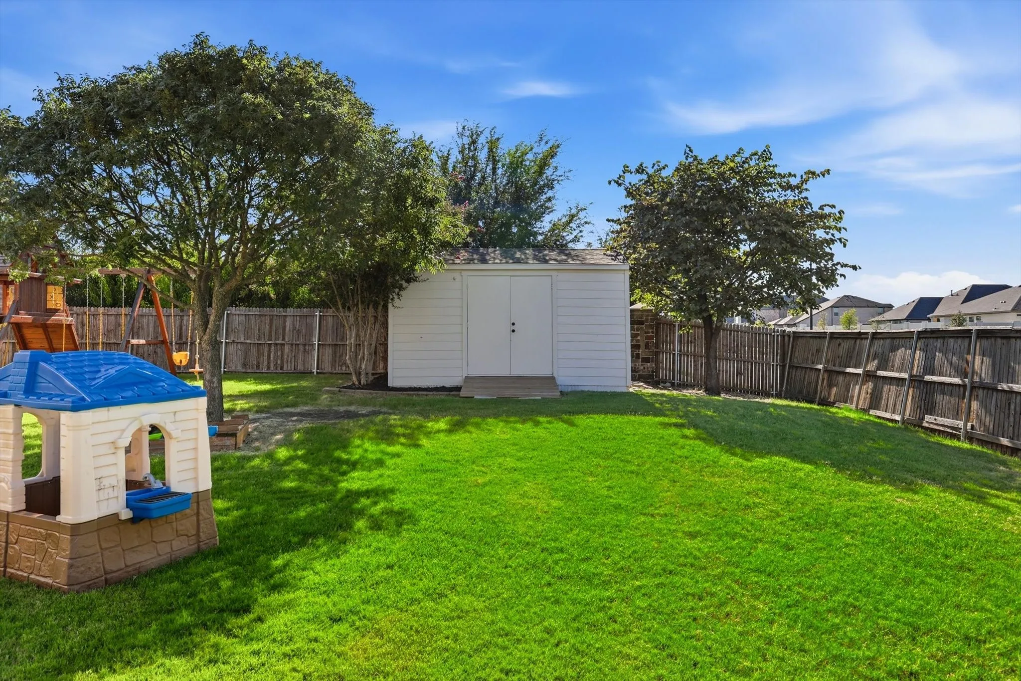 Expansive green lawn featuring a white storage shed, mature trees, and privacy fencing