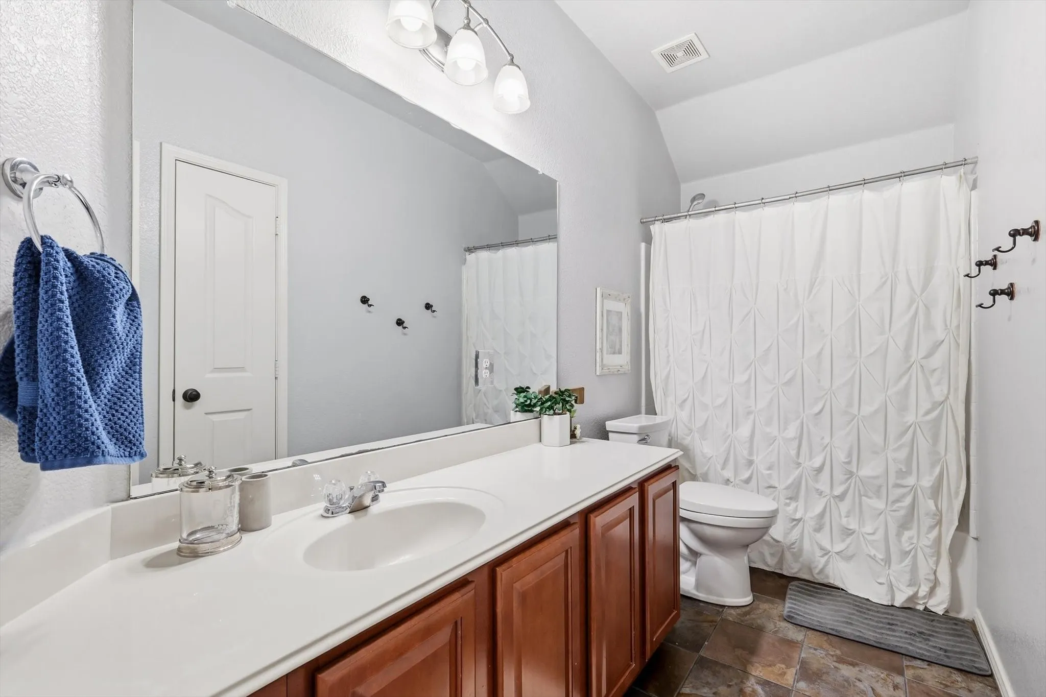 Bathroom featuring a spacious vanity with integrated sink, wood-finish cabinetry, and an expansive wall-mounted mirror