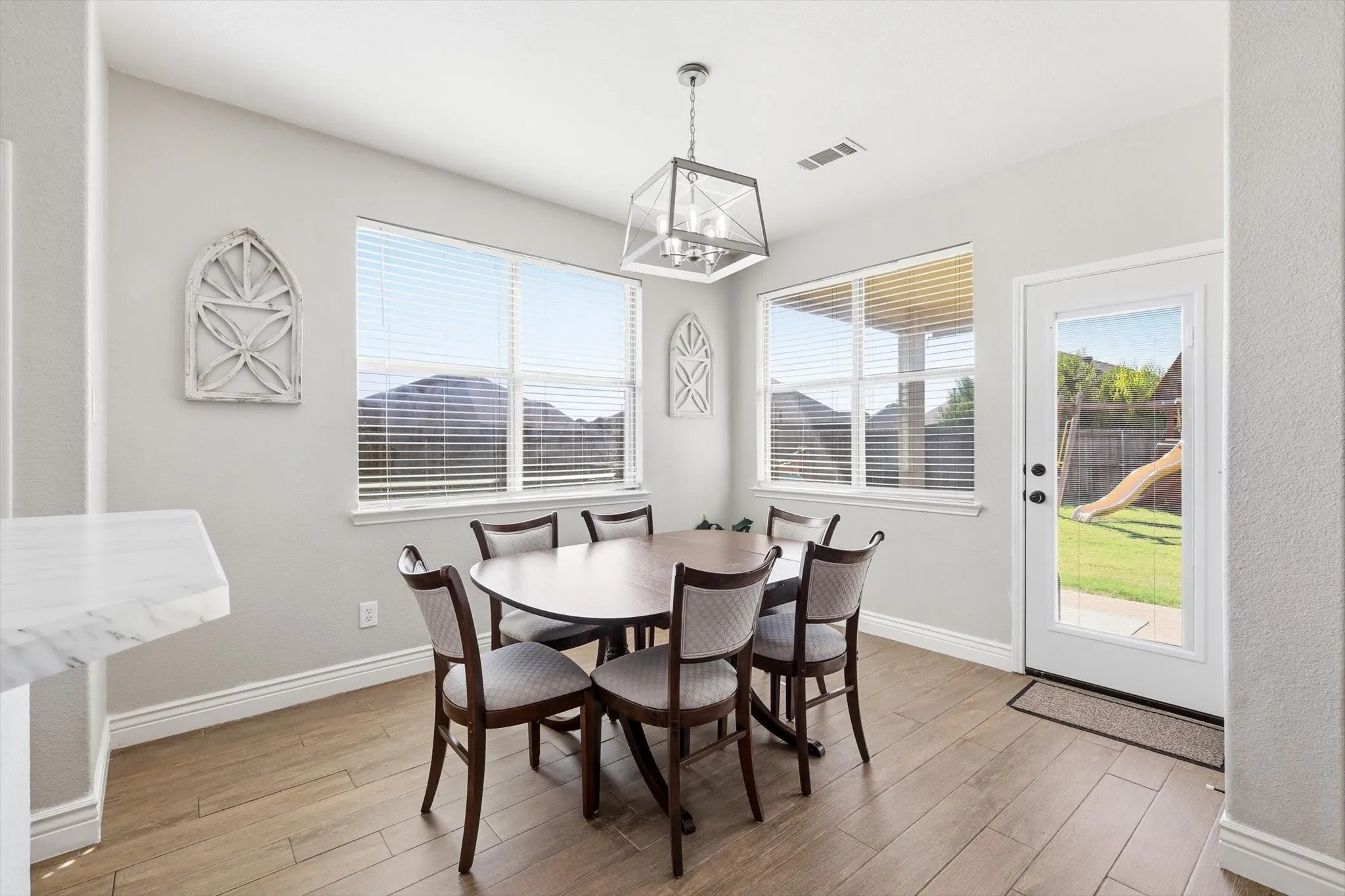 Dining area featuring wood-finish flooring, two large windows with horizontal blinds, and a white glass-paneled door