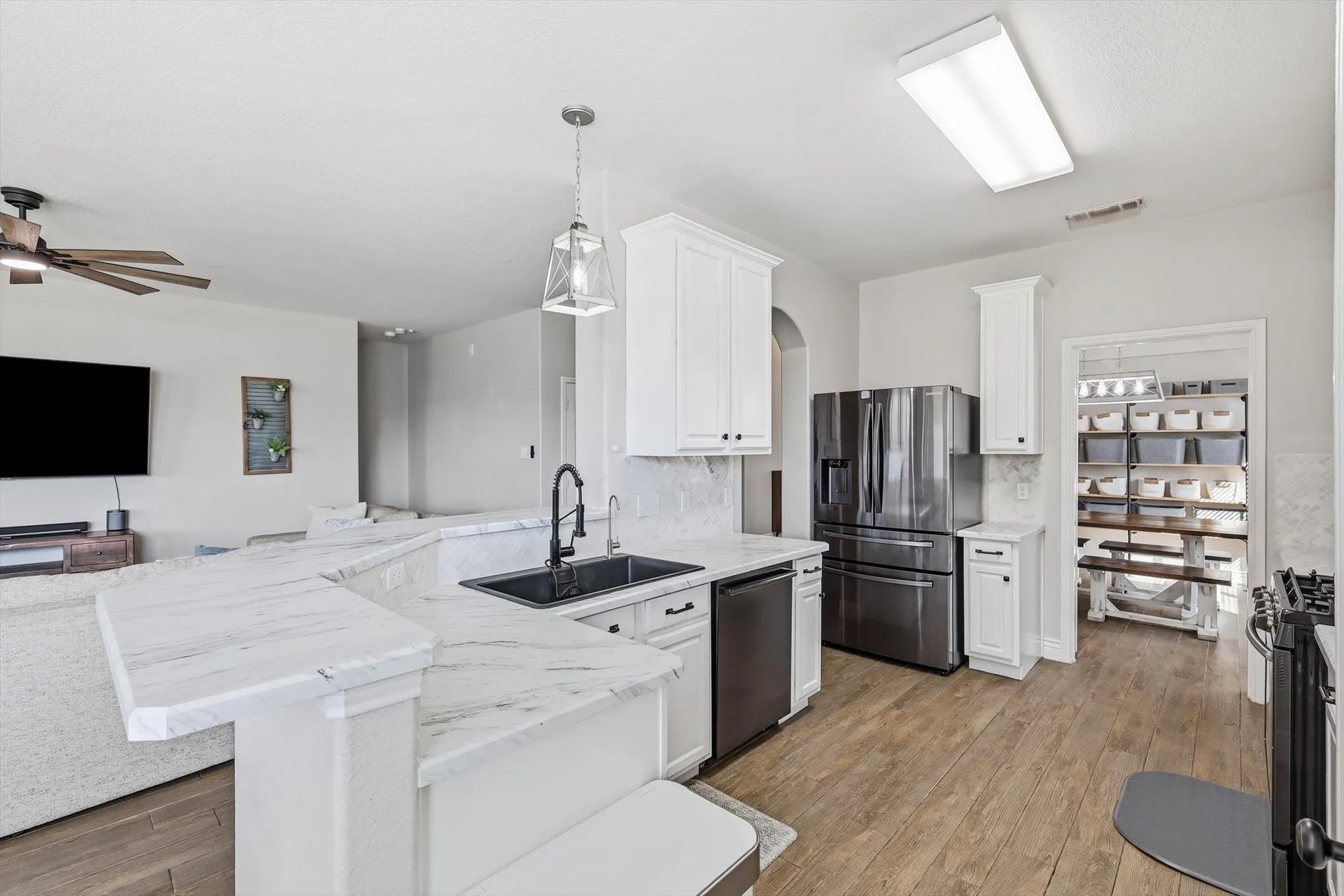 Kitchen featuring wood-finish flooring, white cabinetry, integrated stainless steel appliances, and a spacious pantry with built-in shelving