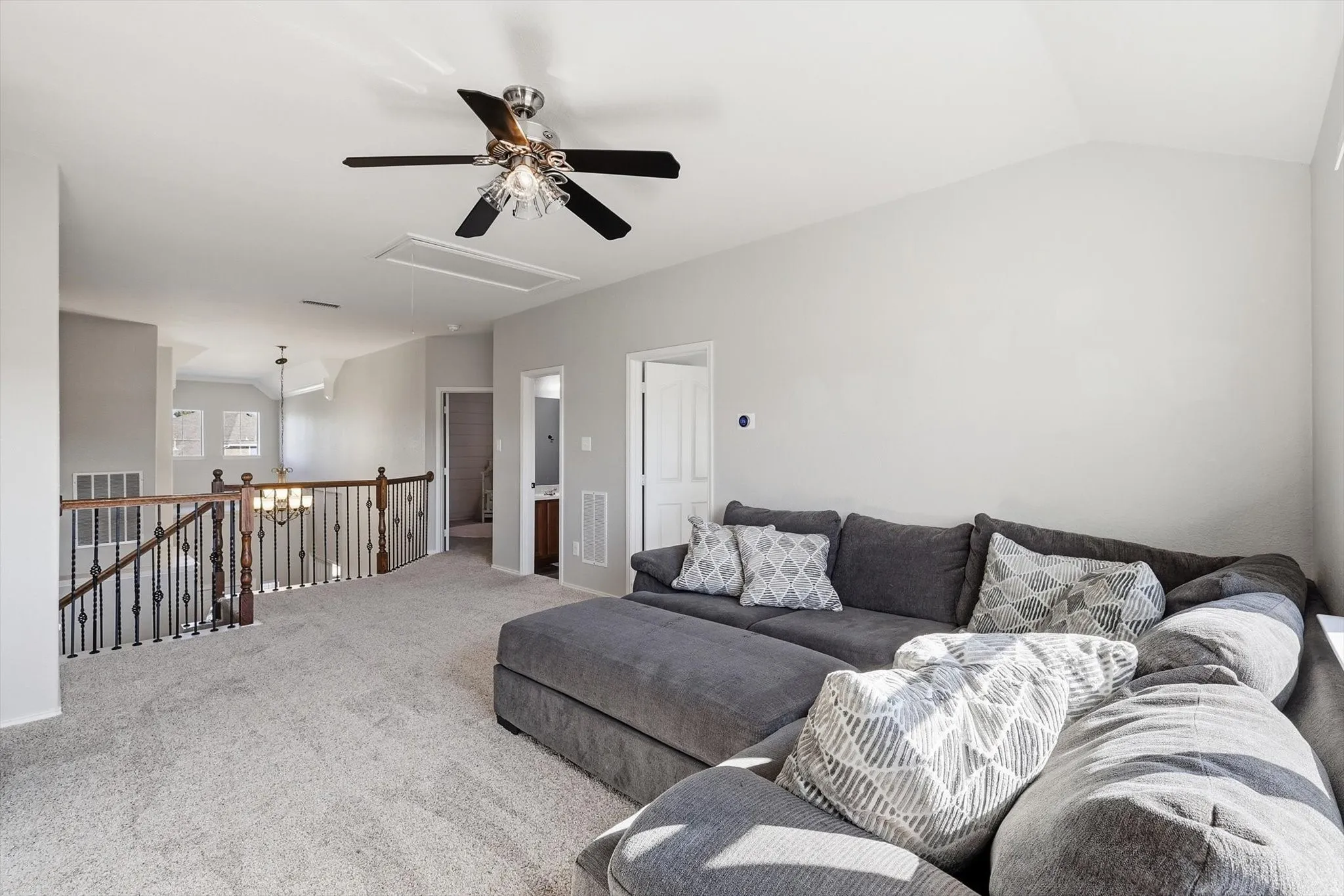 Upstairs Den -Carpeted upper level featuring a vaulted ceiling with a decorative ceiling fan, a railing with dark wood and wrought iron balusters, and light gray wall paint
