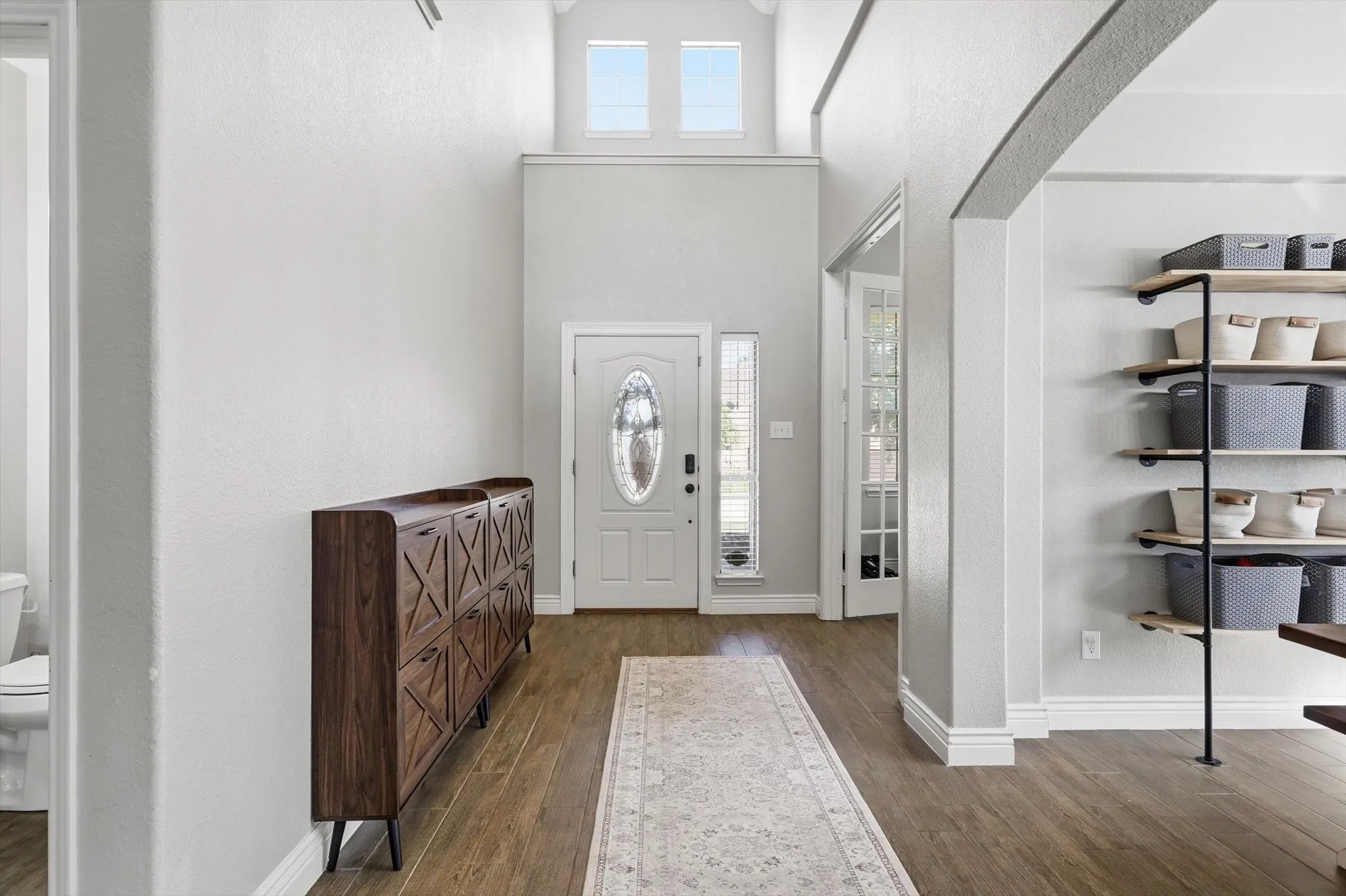 Two-story entryway with wood-finish flooring, a decorative oval-insert front door, and transom windows