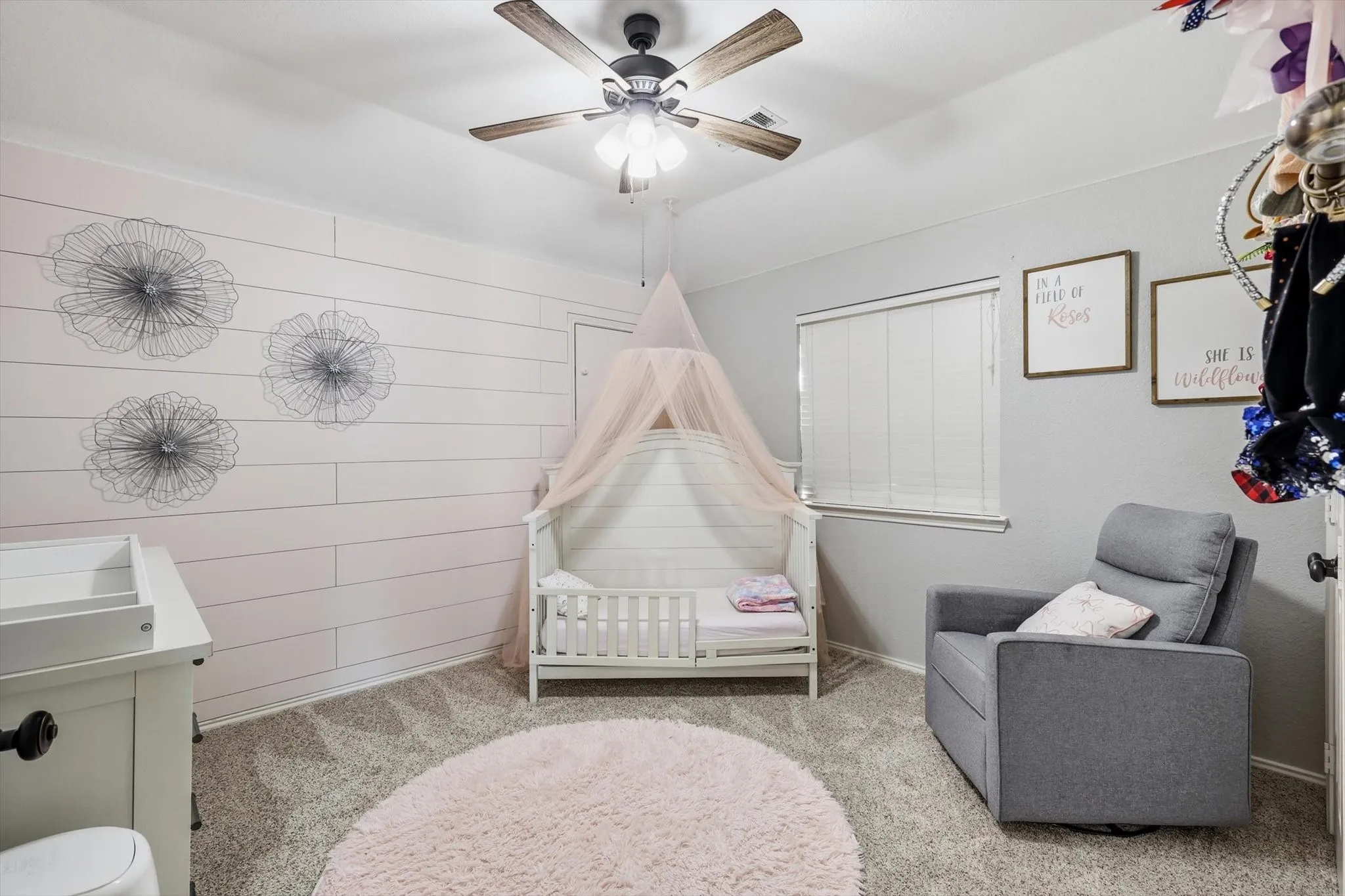 Room featuring a shiplap accent wall, neutral carpeting, and a ceiling fan with light fixture