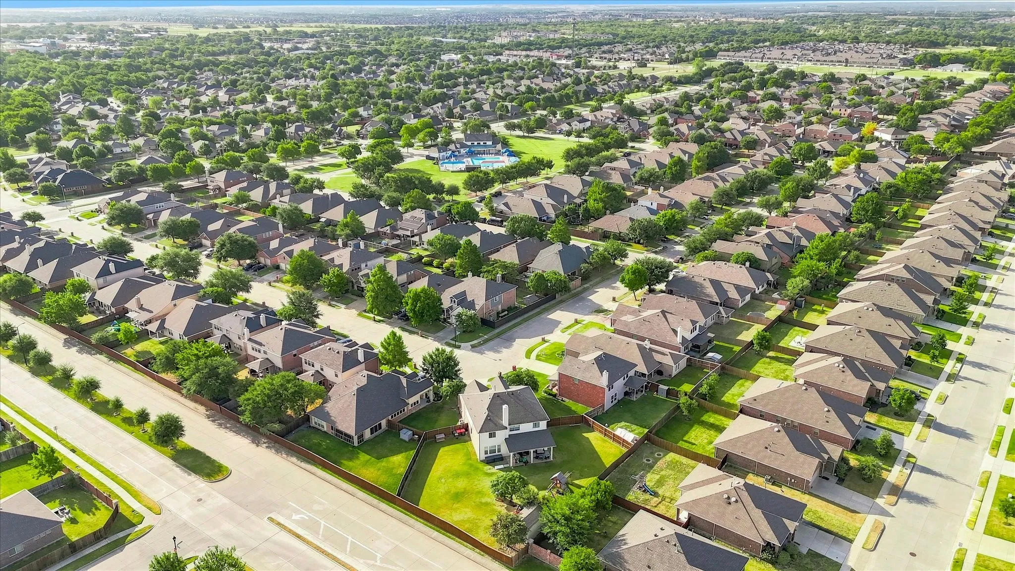 Residential community featuring mature trees, uniform roofing, and paved streets