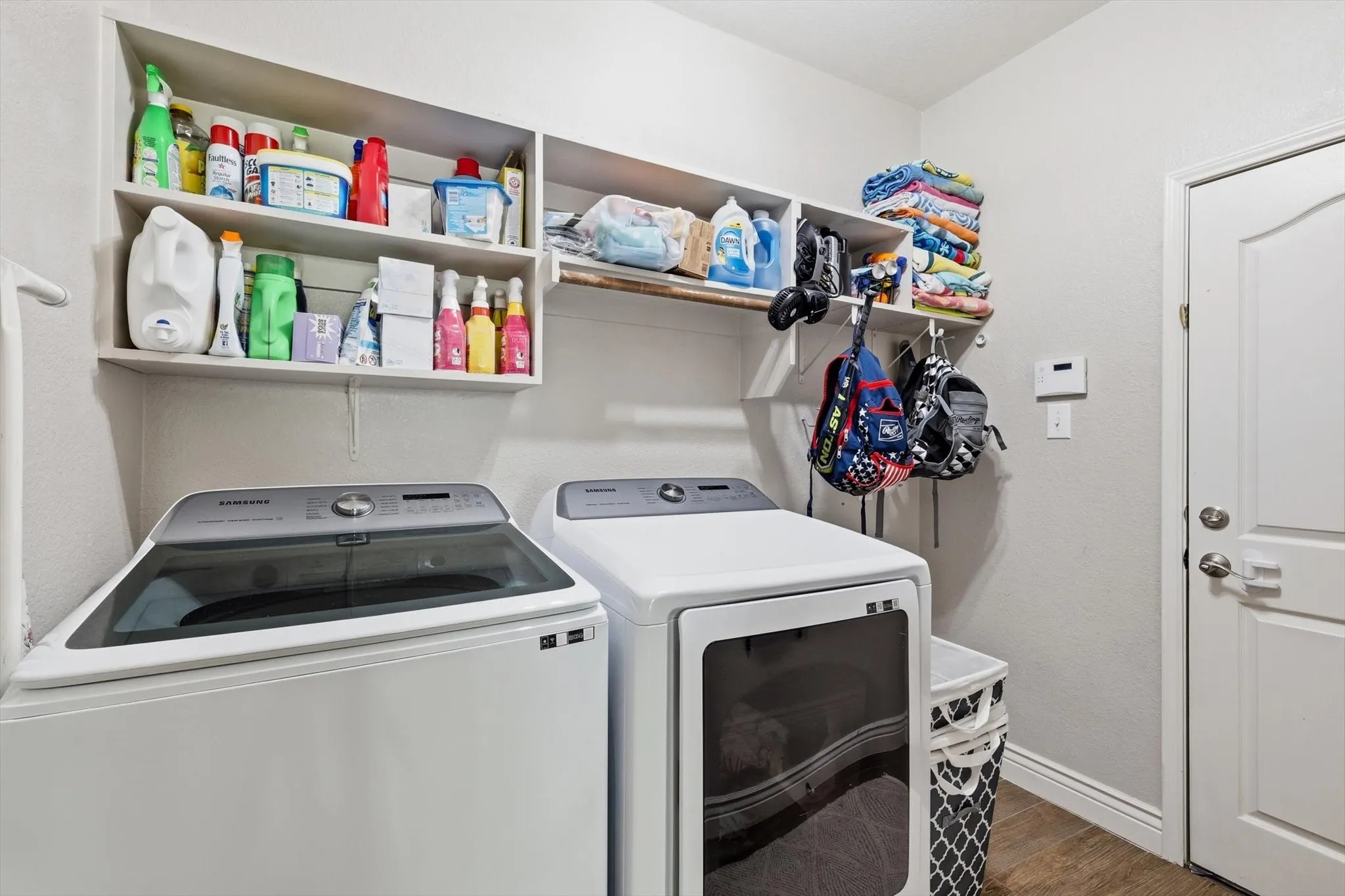 Laundry area featuring wood-finish flooring, white walls, and a white paneled door with brushed nickel hardware