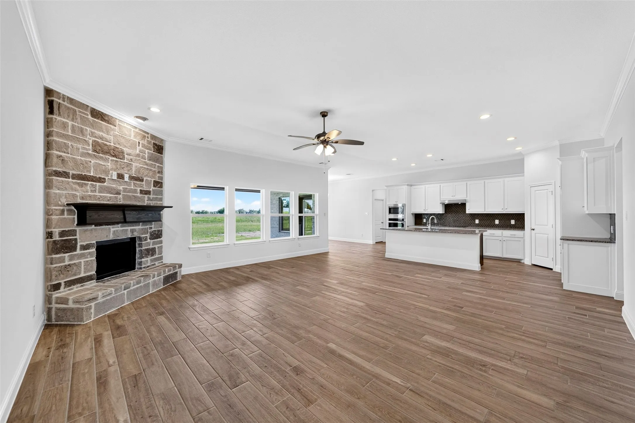 Open concept living space featuring a stone fireplace, wood-finish flooring, and multiple windows