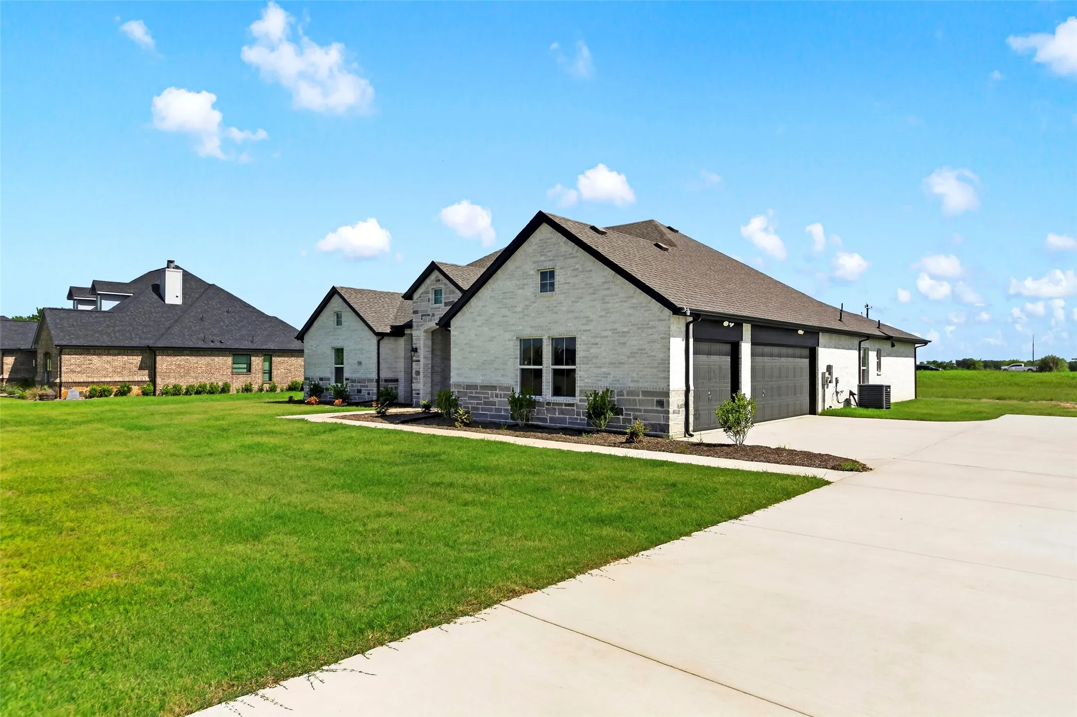 Contemporary single-story home featuring a light-colored brick and stone facade, dark shingle roof, and a two-car garage with dark paneled doors