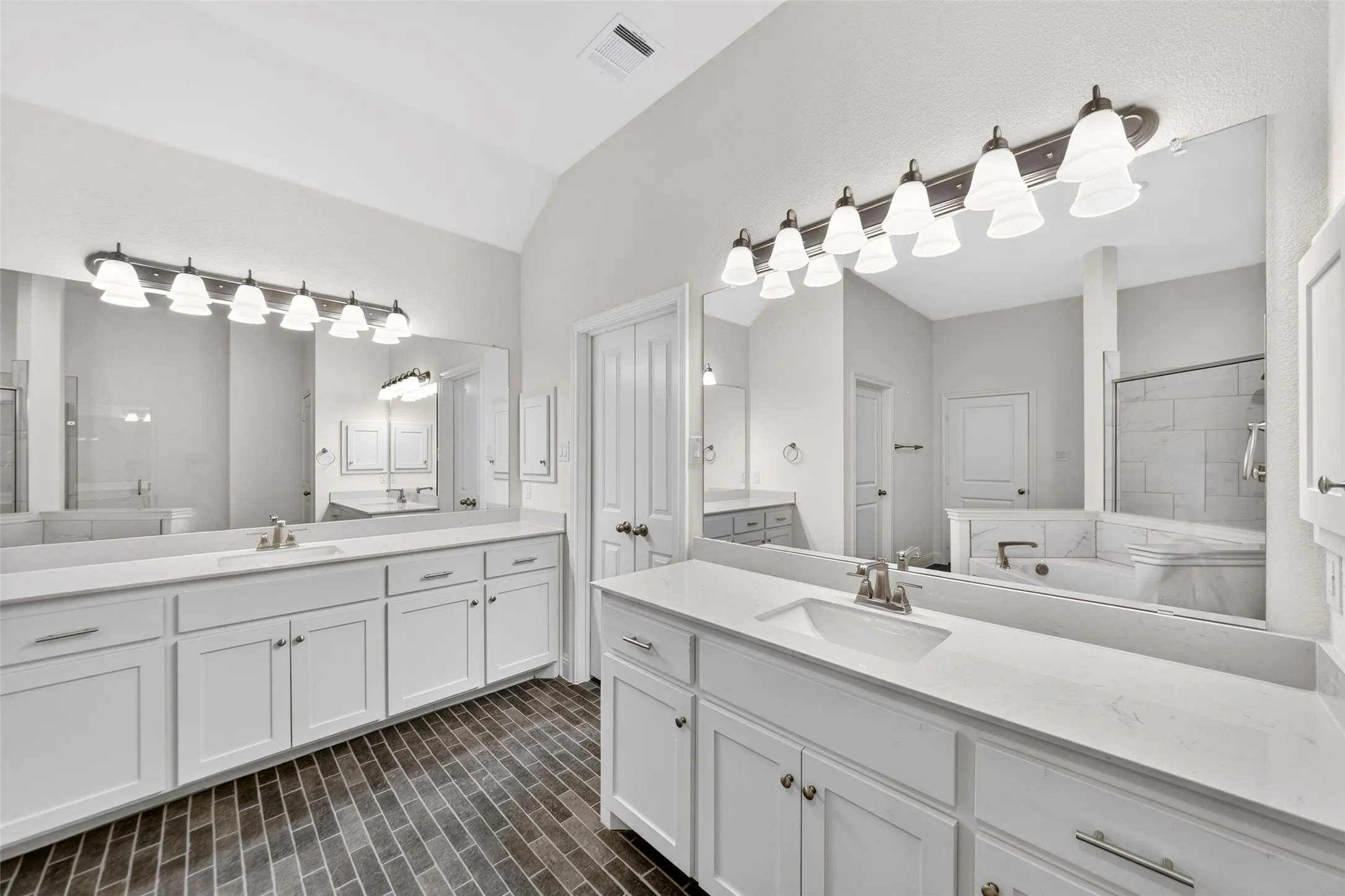 Bathroom featuring dual white vanities with integrated sinks and quartz countertops, illuminated by multi-bulb vanity lighting