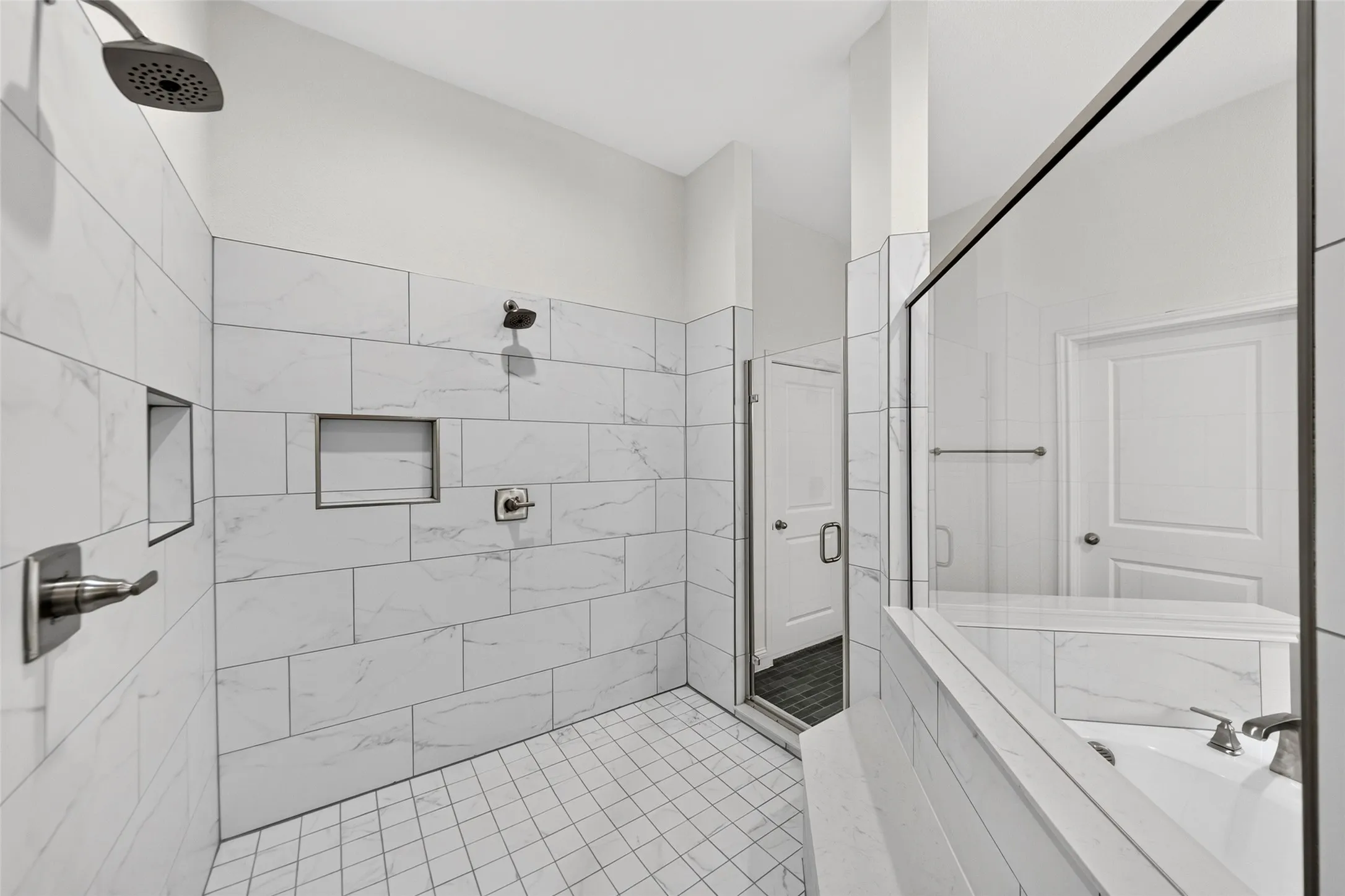 Spacious walk-in shower featuring large format marble-look tile, built-in shower niches, and an overhead rain shower