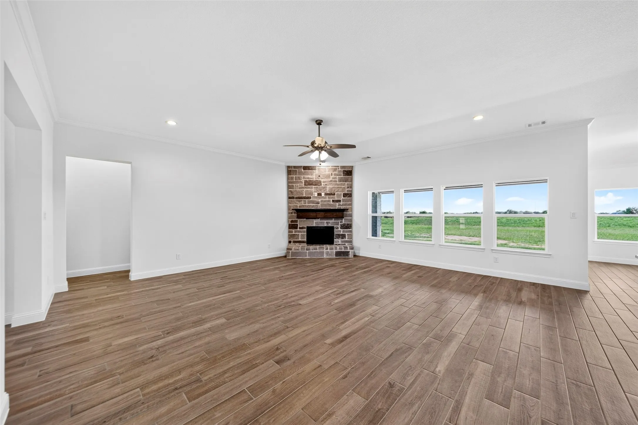 Spacious living area featuring wood-finish tile flooring, a stone-clad fireplace with a wood mantle, and a ceiling fan with light fixture