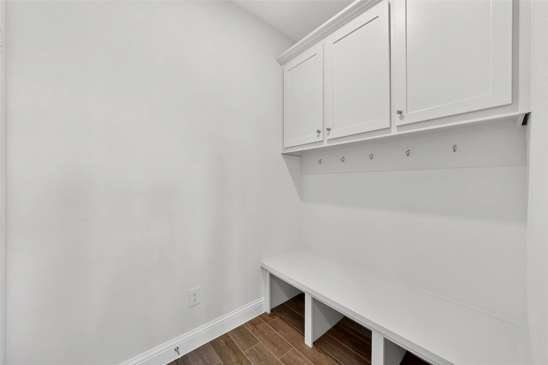Built-in white cabinetry with chrome hardware, integrated bench seating, wall-mounted hooks, and wood-finish flooring
