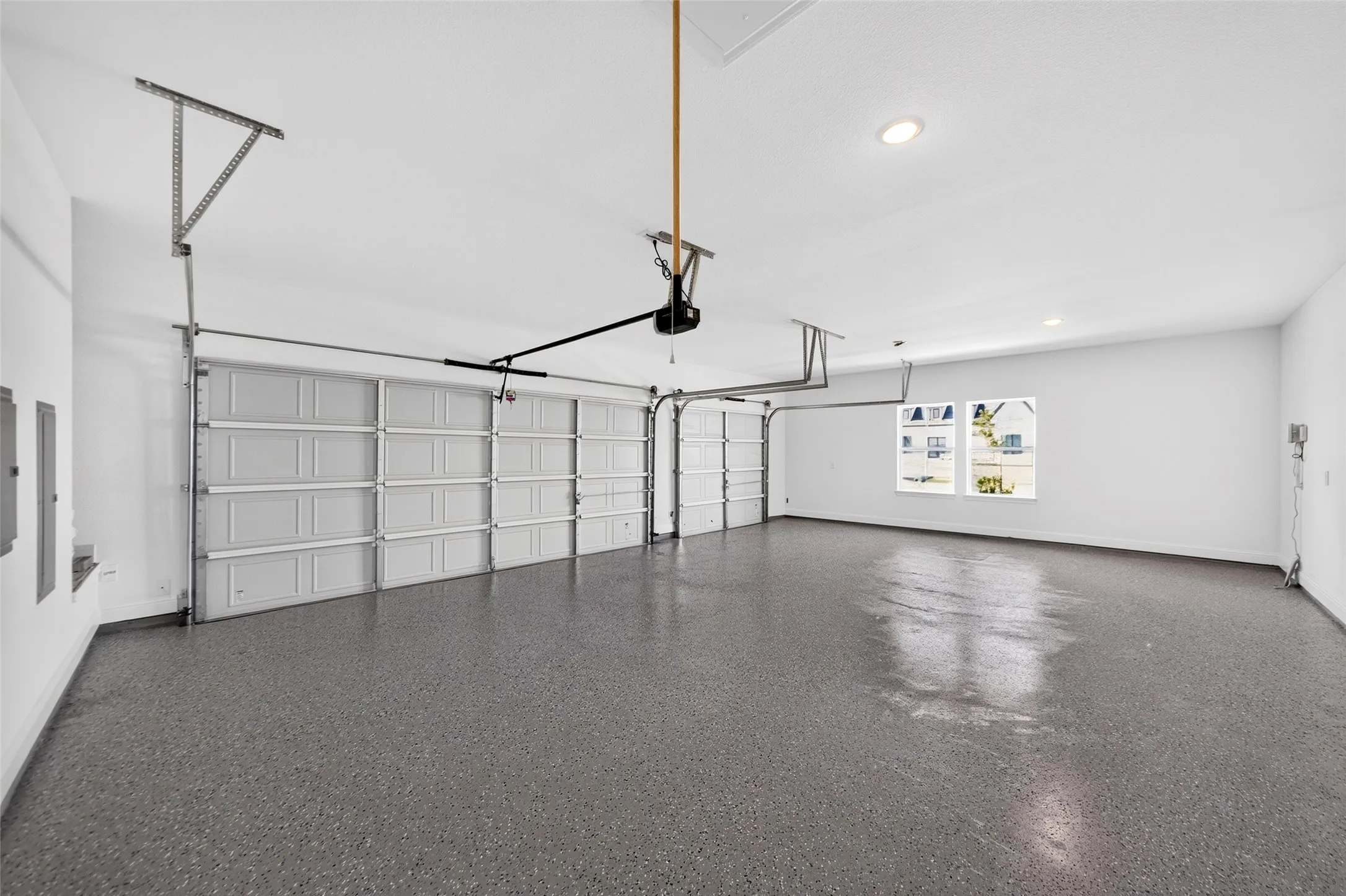 Spacious garage featuring a durable epoxy floor finish, two overhead garage doors, recessed lighting, and a double window