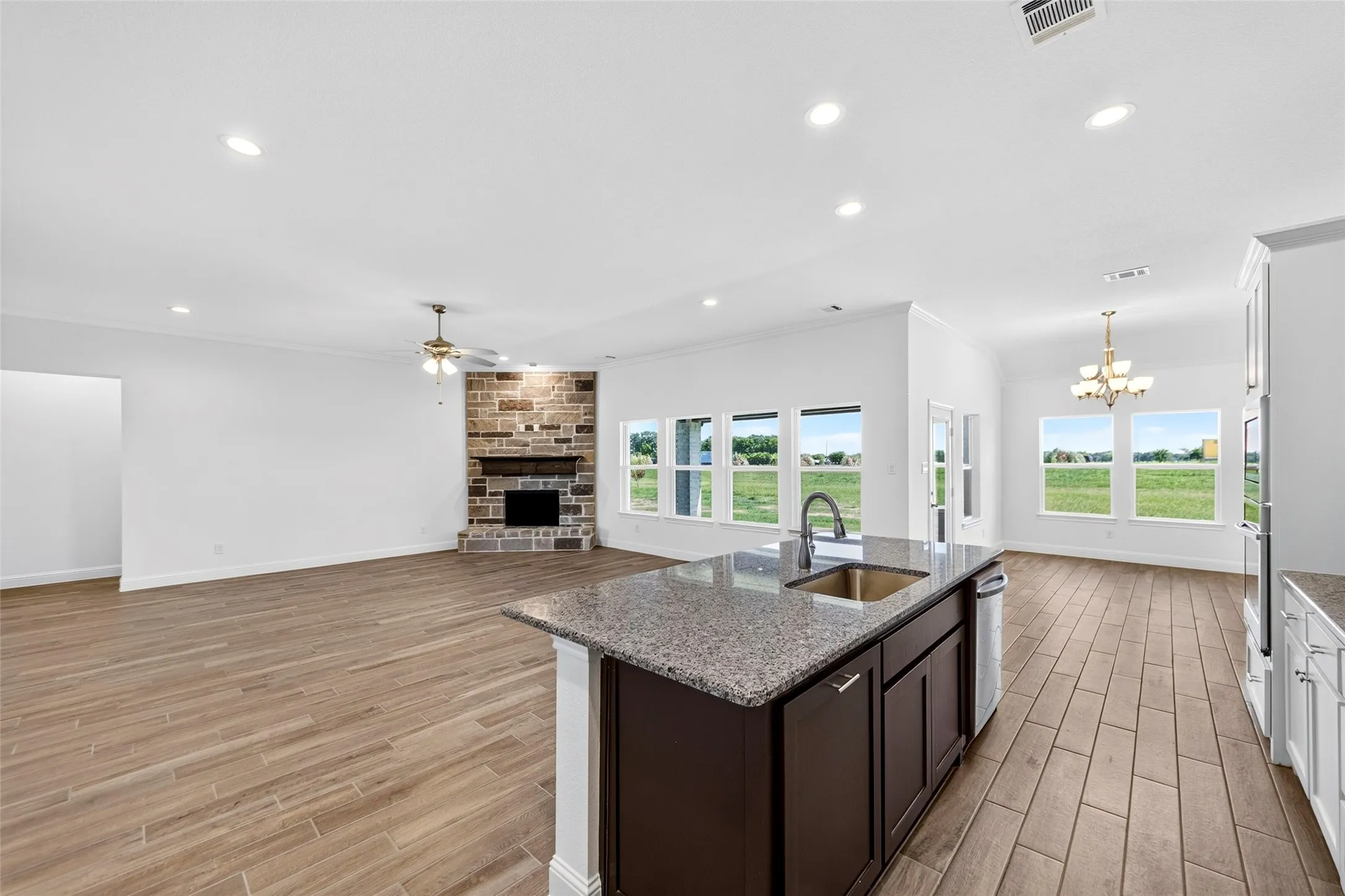 Open-concept living area with wood-finish flooring, a stone fireplace, and multiple windows