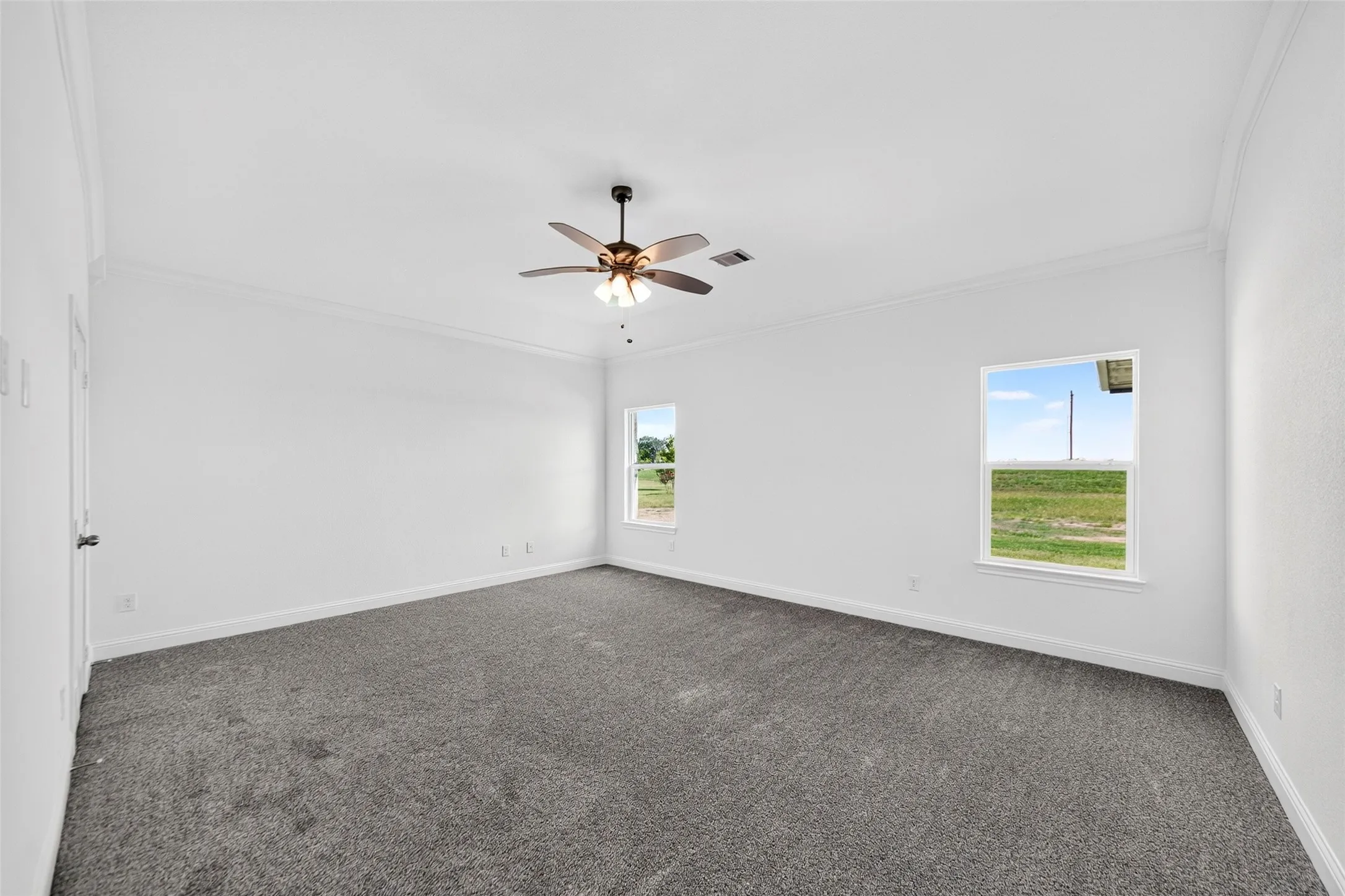 Spacious room featuring neutral carpeting, white walls, two windows, crown molding, and a ceiling fan