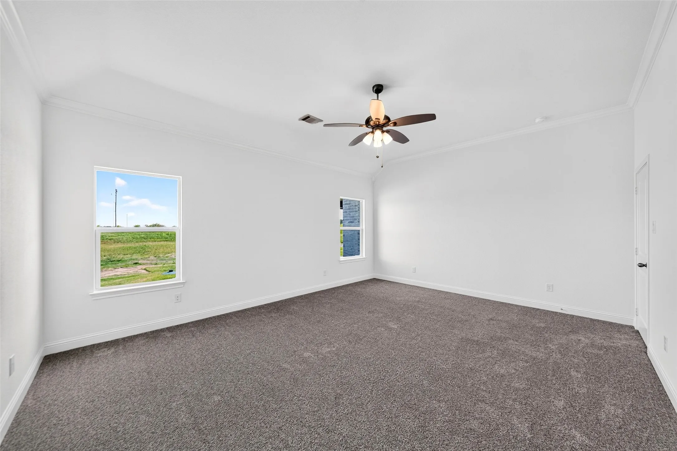 Spacious room featuring vaulted ceilings, neutral-toned carpeting, two windows, and a ceiling fan with integrated lighting