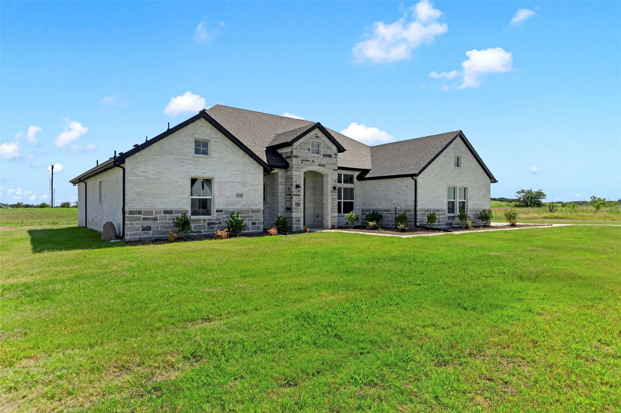 Single-story residence featuring a light brick exterior with stone accents and a dark shingle roof